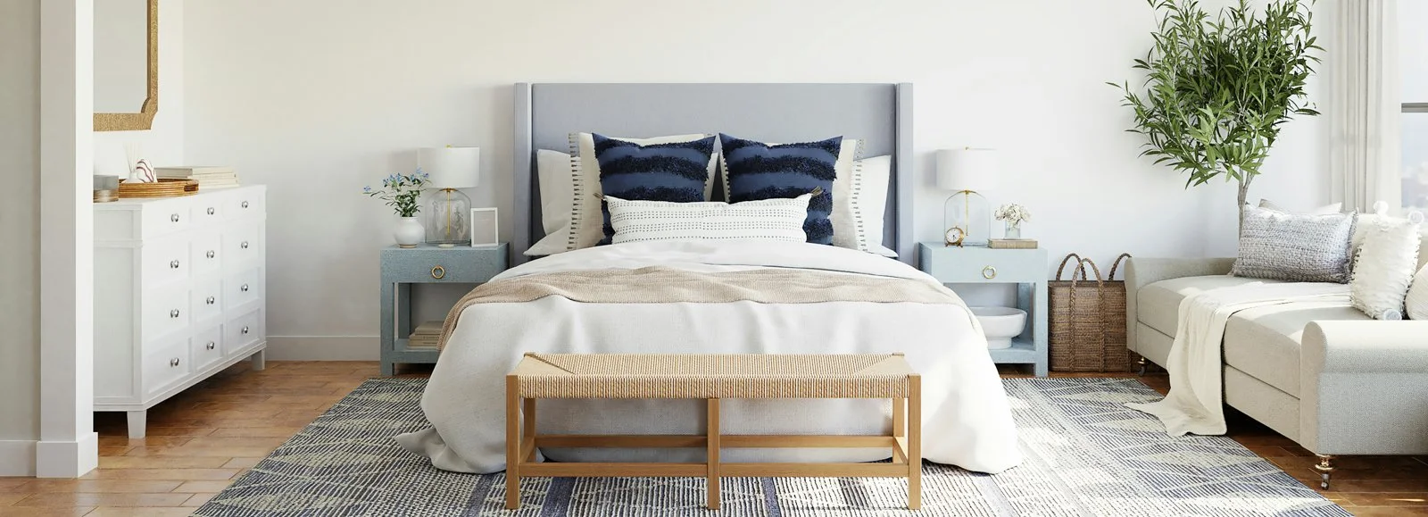 Photo of a bed with a white comforter and  navy blue pillows with a woven bench at the foot at Box Drop Alexandria, LA.