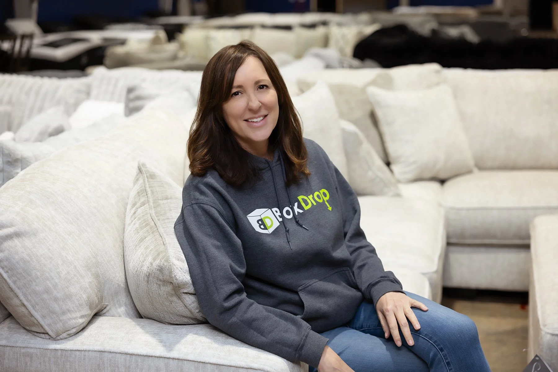 Owner of Box Drop sitting on a linen couch at Box Drop Alexandria, LA, wearing a grey Box Drop sweatshirt.