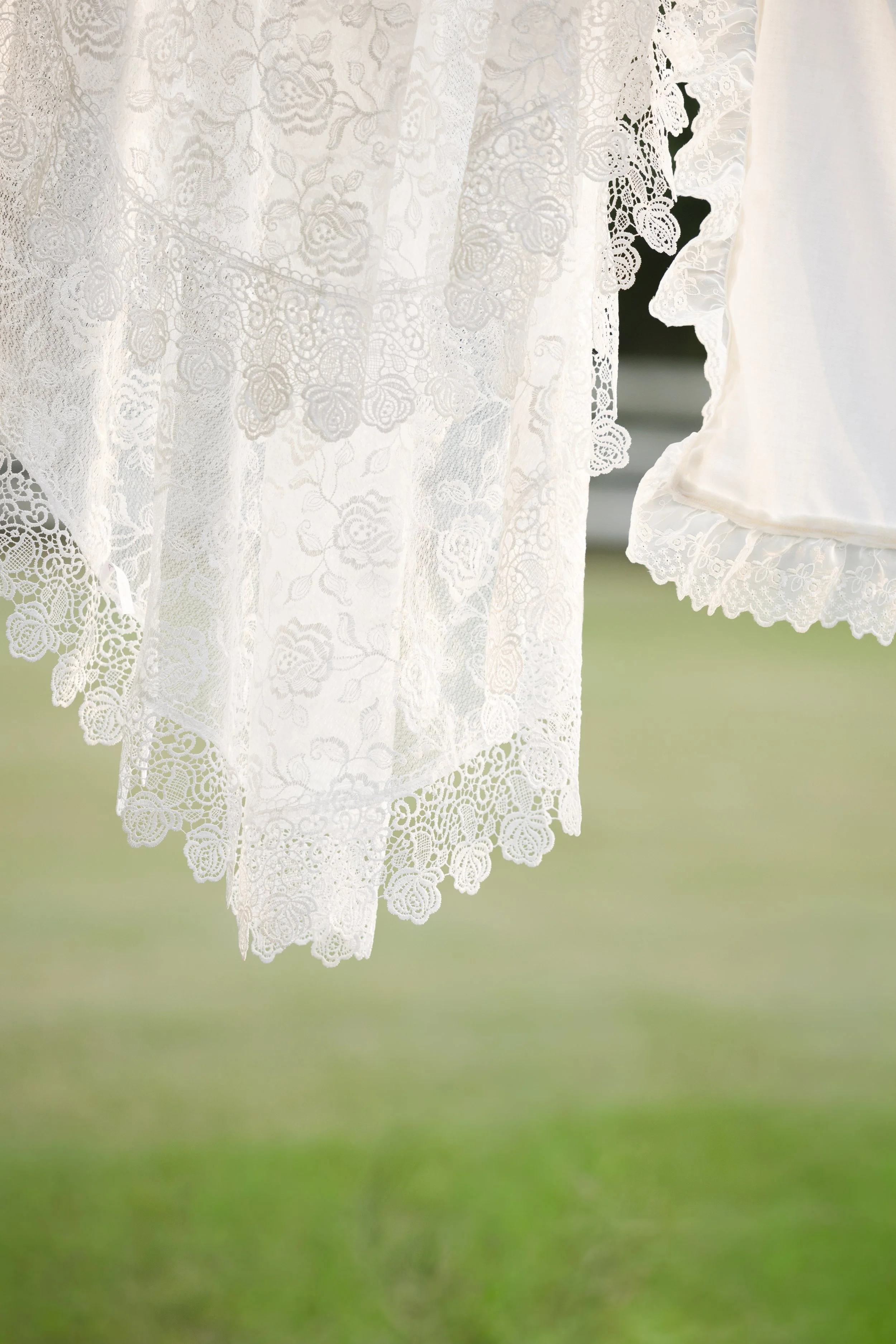 Close-up of white floral lace fabric with scalloped edges against a blurred green background