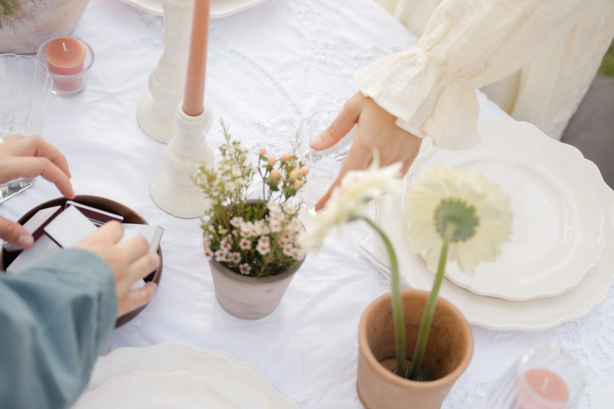 Elegant white table setting with candles, flowers, plates, and hands arranging place cards