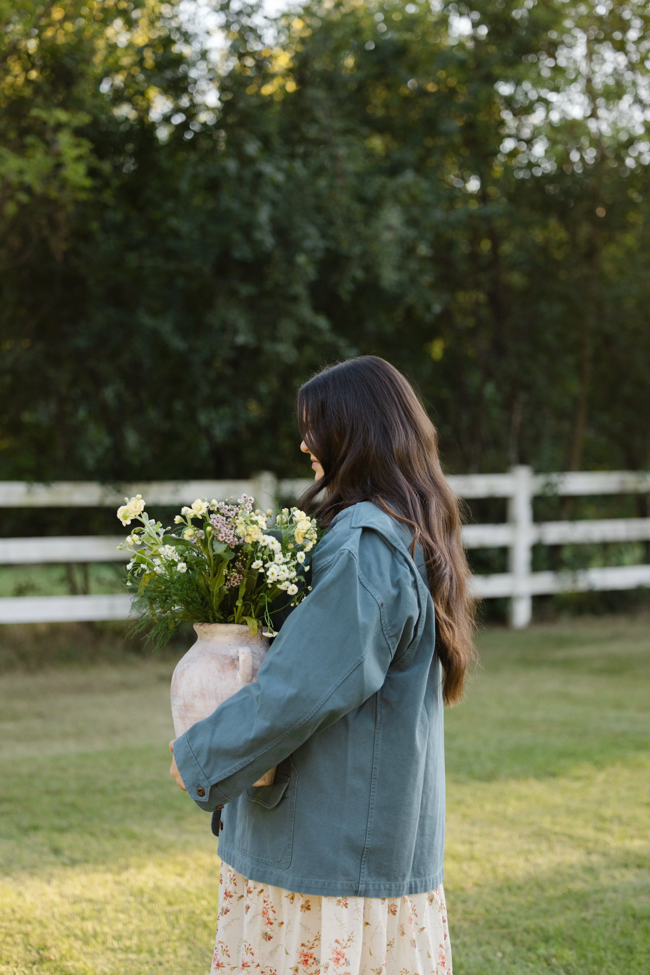 Woman in a blue jacket holding a vase of wildflowers outdoors