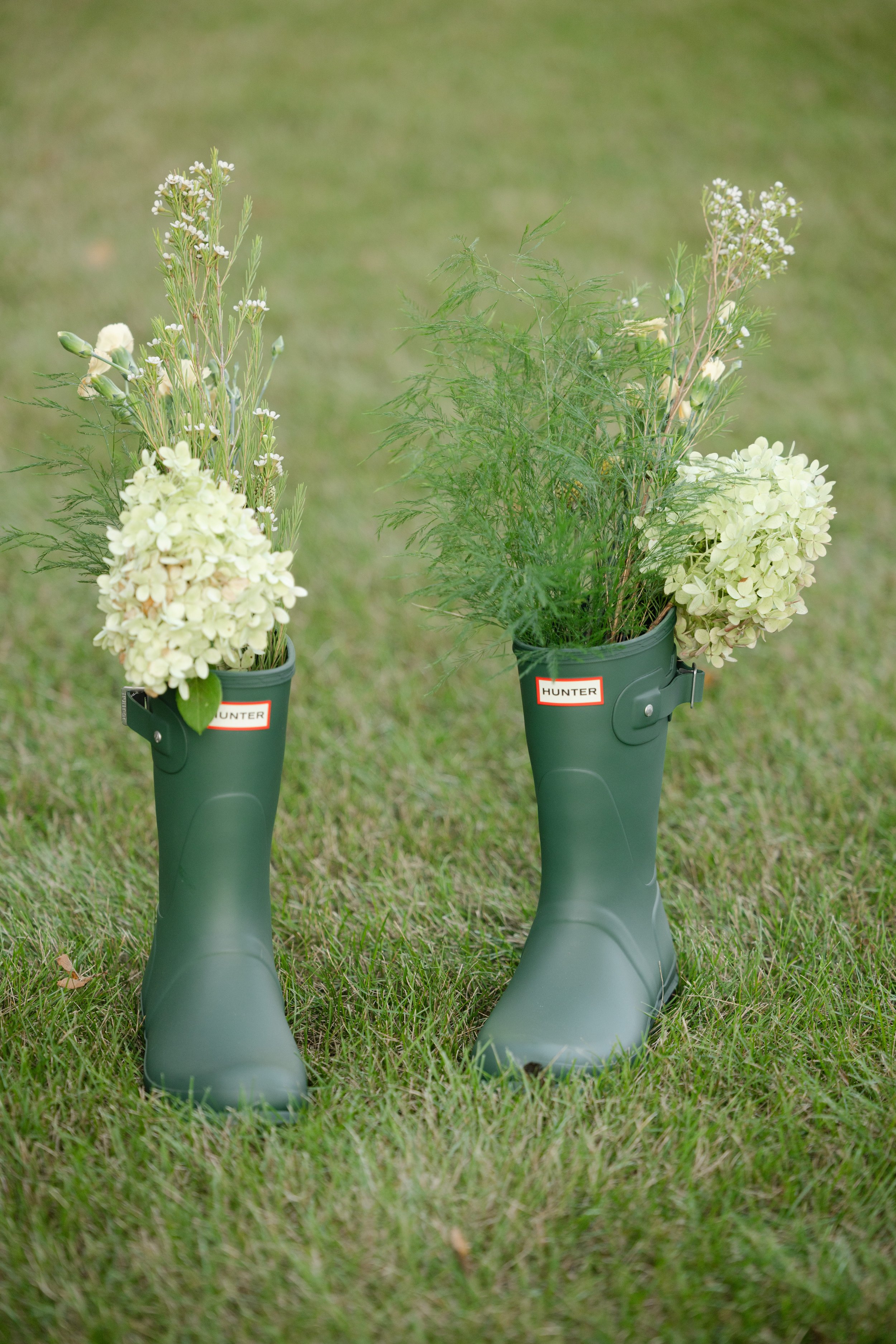 Green Hunter rain boots filled with white flowers and greenery, standing on grass