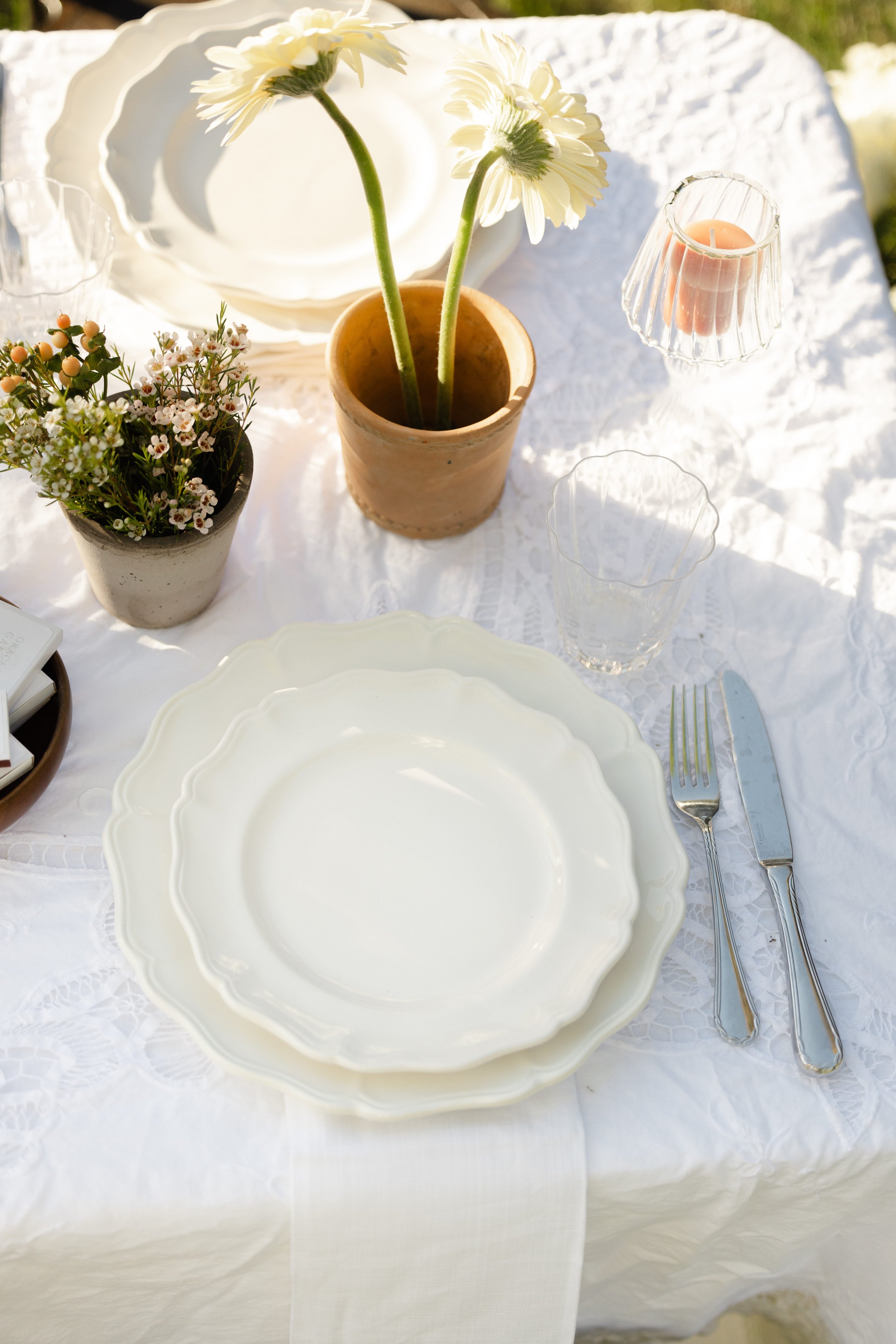 Elegant outdoor table setting with white plates, silverware, candles, and potted white flowers