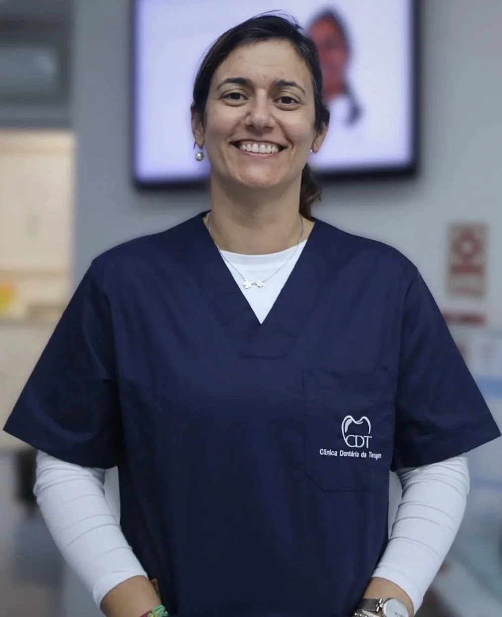 Mulher sorridente usando uniforme azul de dentista na clínica odontológica.