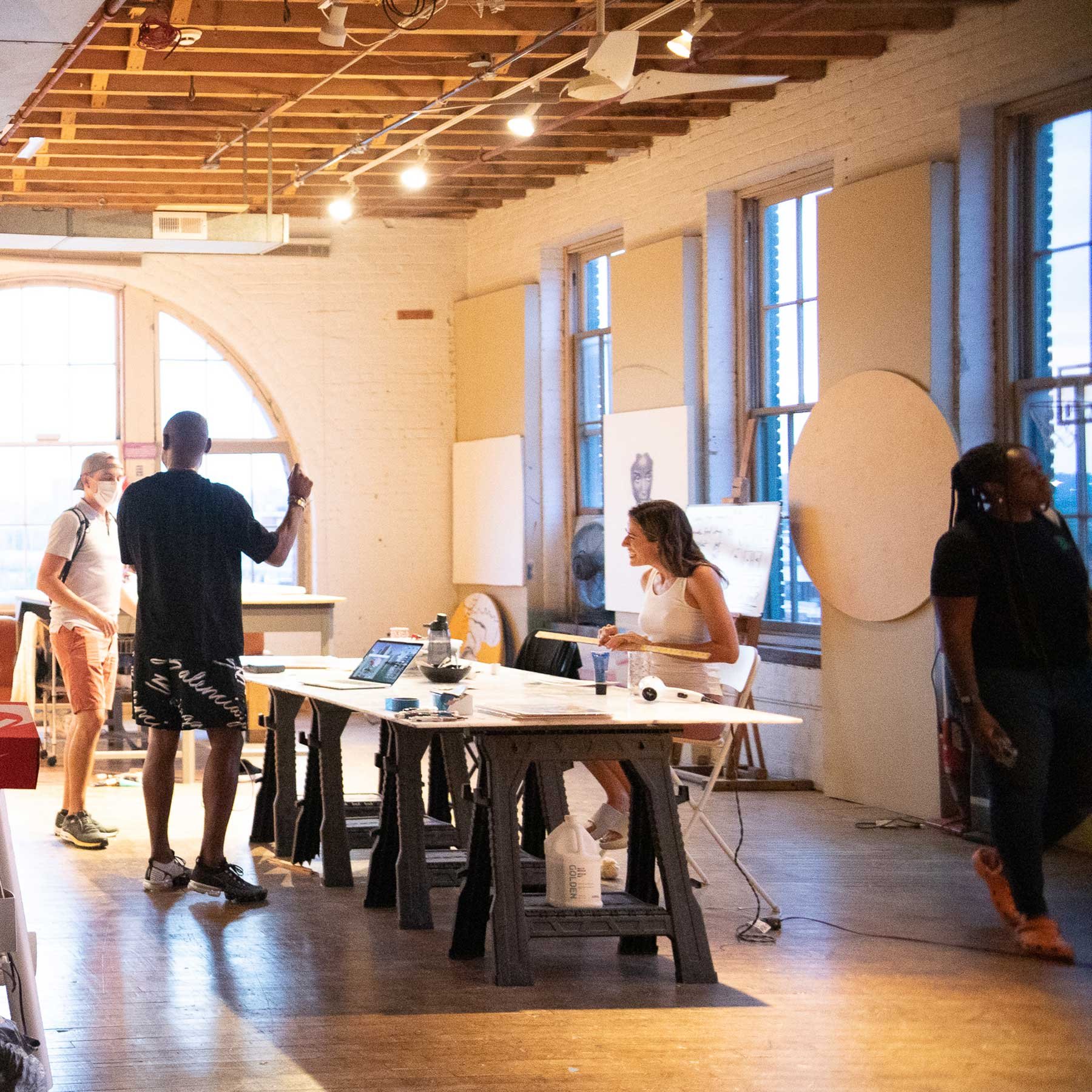 People in an art studio working together with paintings and materials on tables.