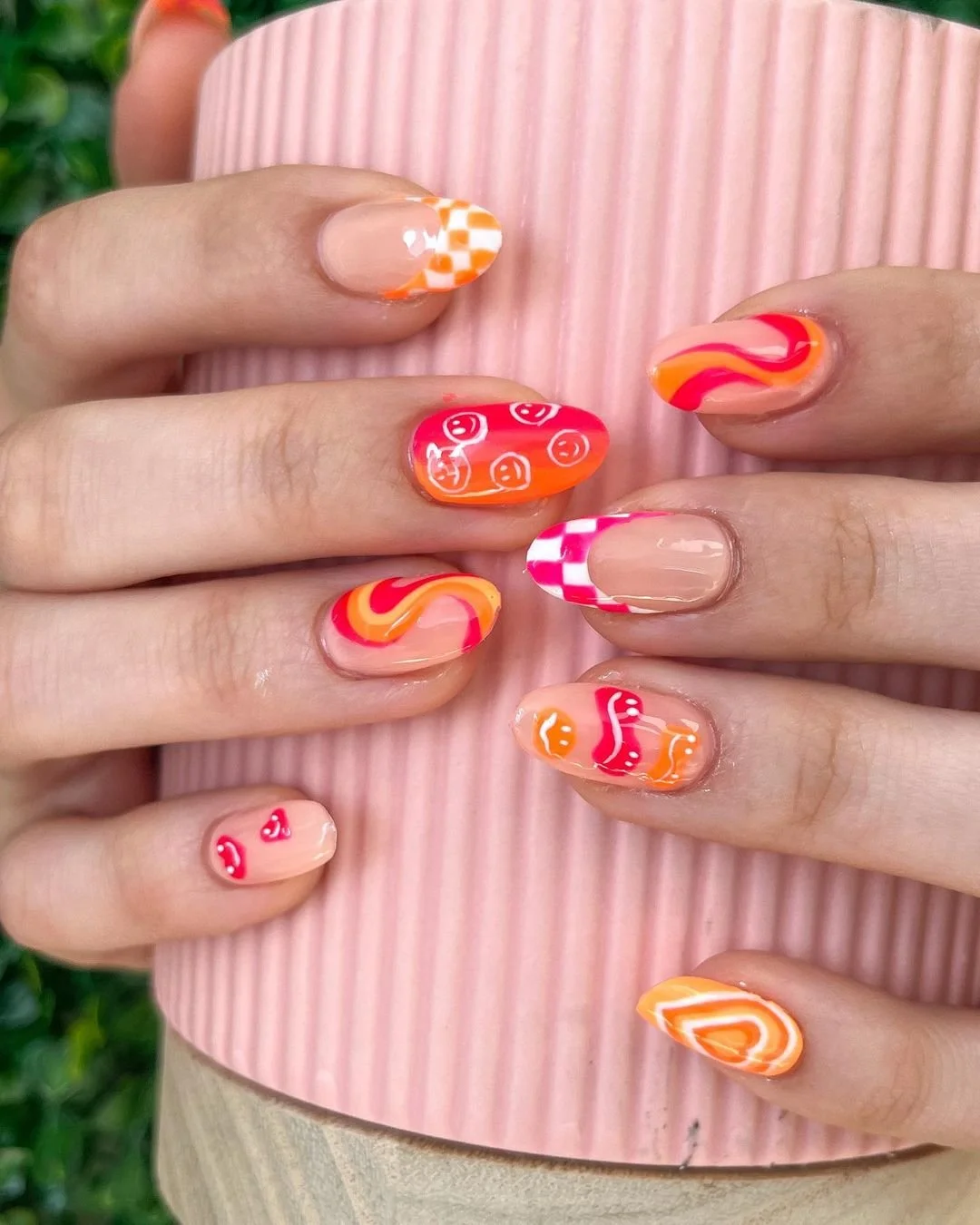 Colorful, patterned nail art on fingernails with a pink, textured background.