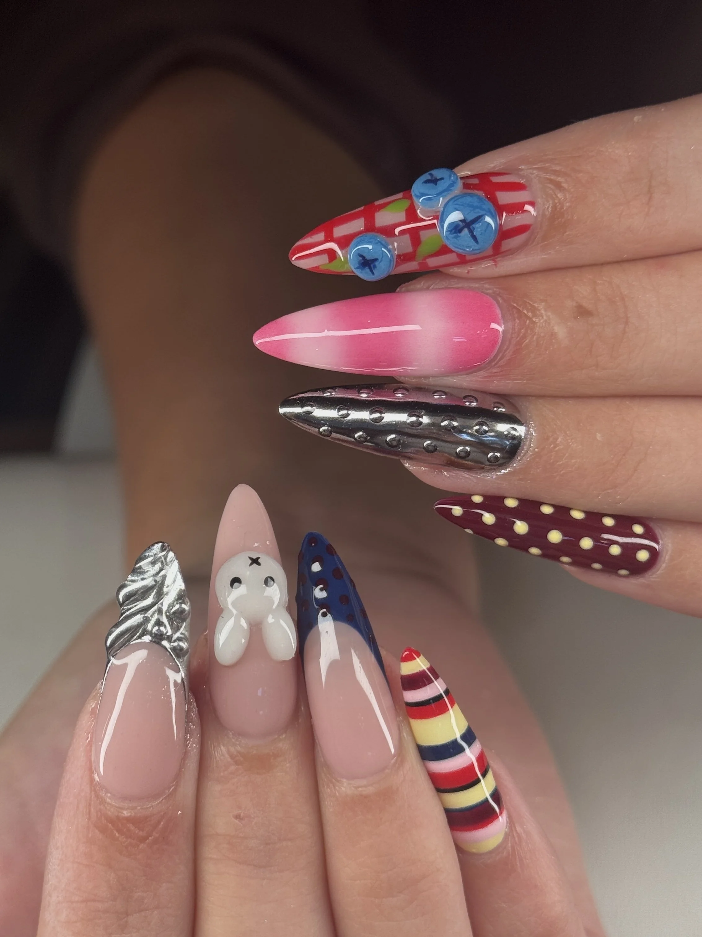 Close-up of colorful, decorated artificial nails with various patterns and 3D embellishments.