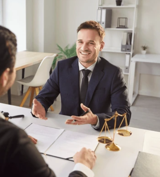 A man in a suit and tie smiling and talking during a legal consultation or interview in an office setting.