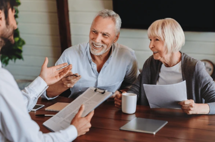 An elderly couple engaged in a conversation with a professional, possibly a financial advisor, in a cozy office setting.