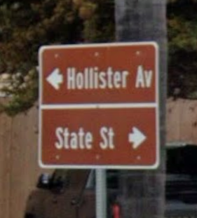 a blurry photo of a directional street sign showing a left arrow and Hollister Av on top, and State St with a right arrow on the bottom.