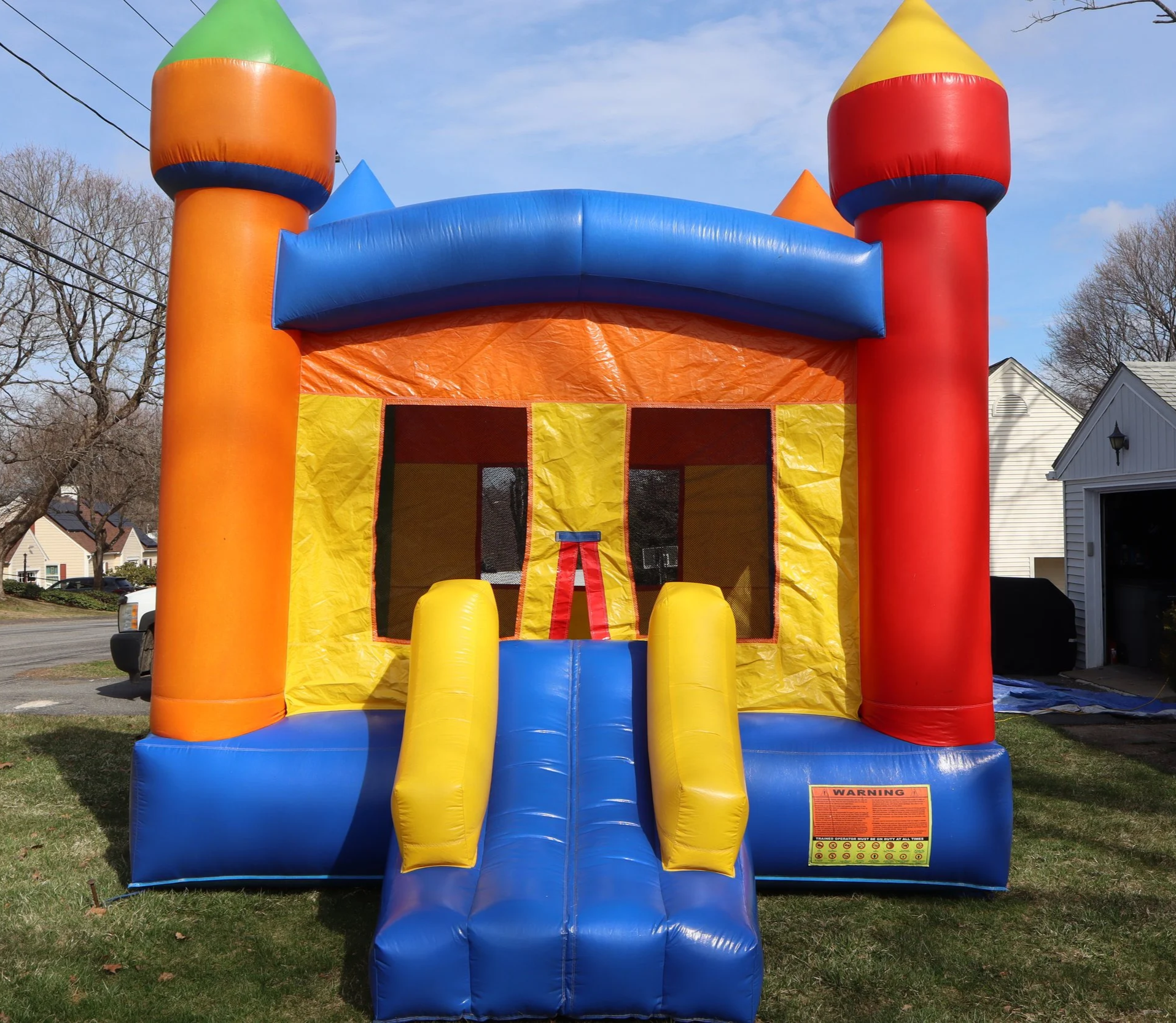 Colorful inflatable bounce house with a castle design, featuring red, yellow, blue, green, and orange sections, set up outdoors on a grassy yard during daytime.