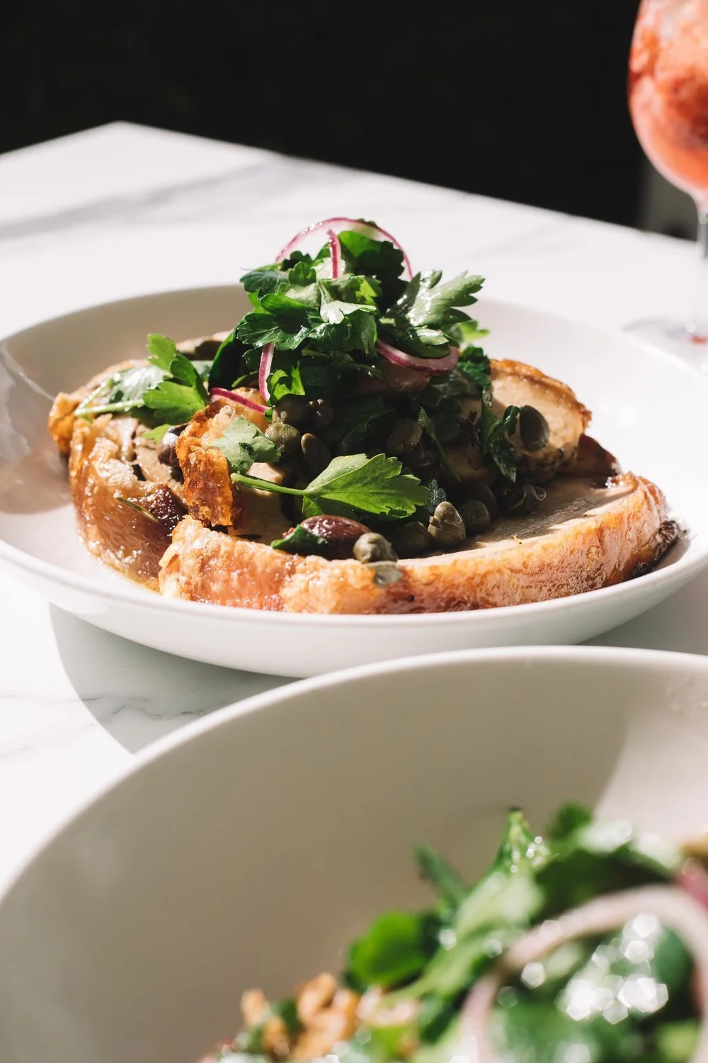 Plate of roasted pork with greens, capers, and red onion garnish