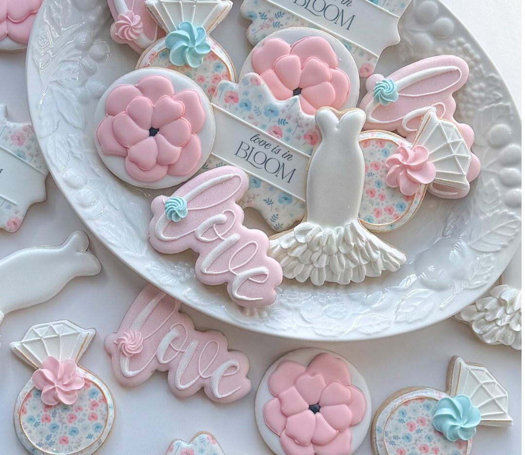 Decorated cookies with floral, love, and wedding theme on a white plate.