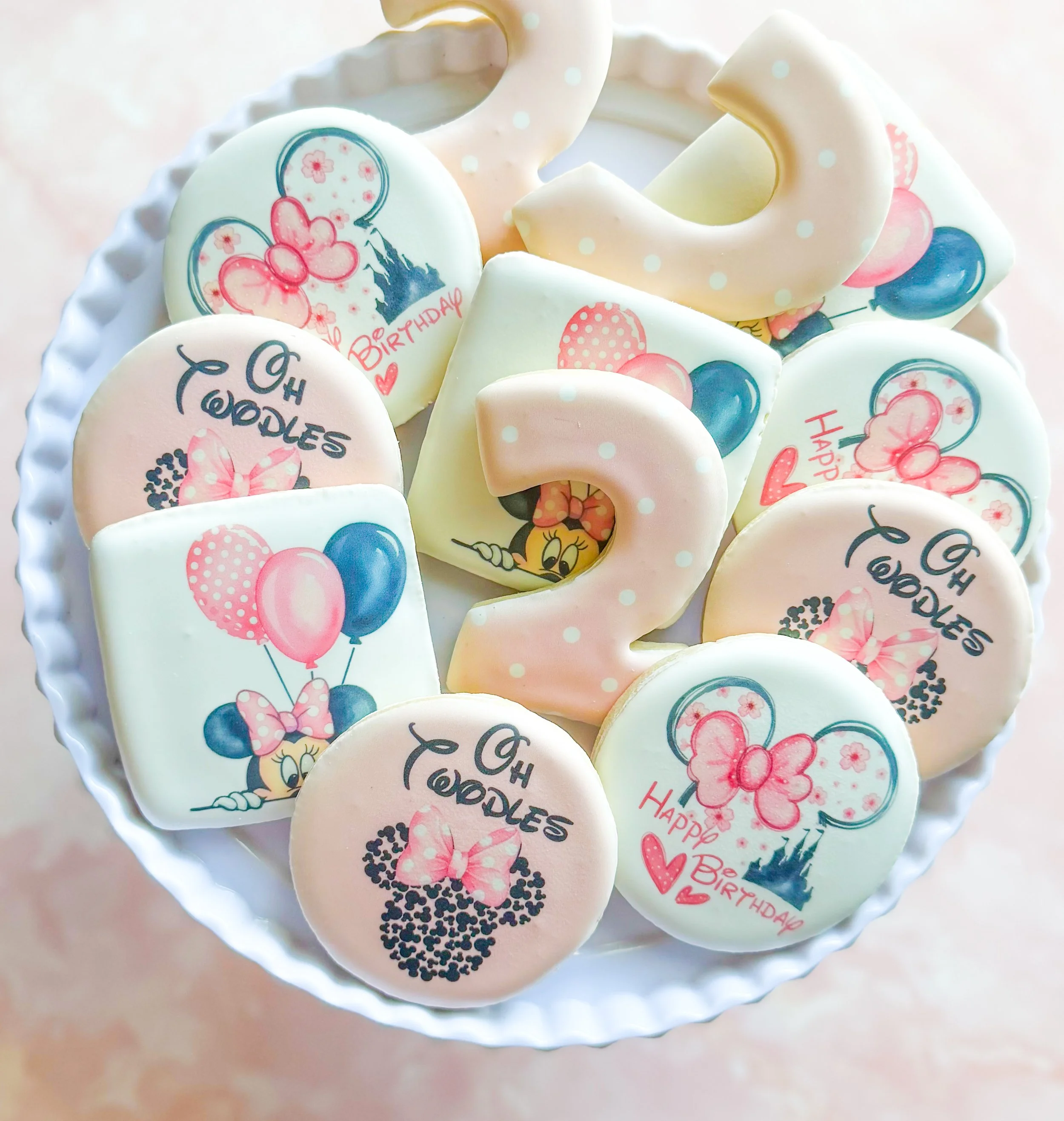 Decorative cookies with birthday messages and cartoon princess images arranged in a white dish.