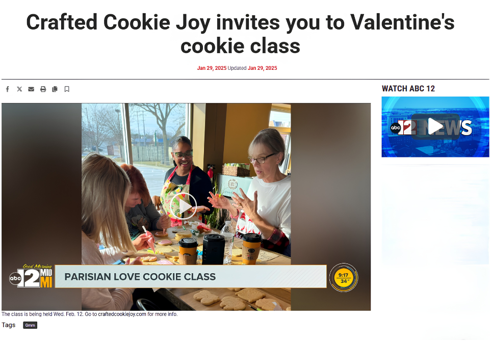 A group of women participating in a cookie decorating class at a table with cookies, coffee cups, and ingredients, with large windows in the background letting in natural light.