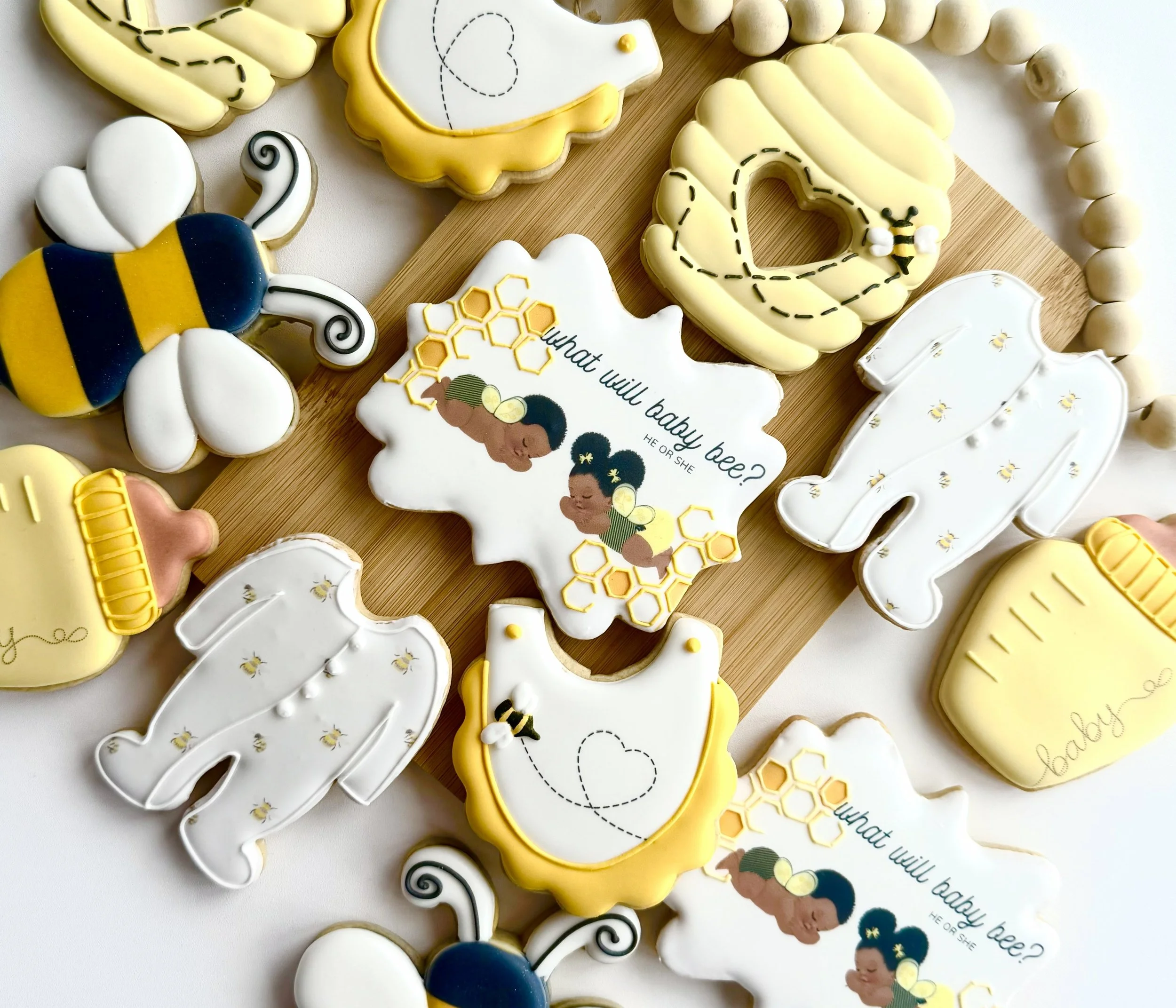 Decorated cookies with baby and bee themes, including honey jars, bees, and a cookie with the text 'What will baby bee?'
