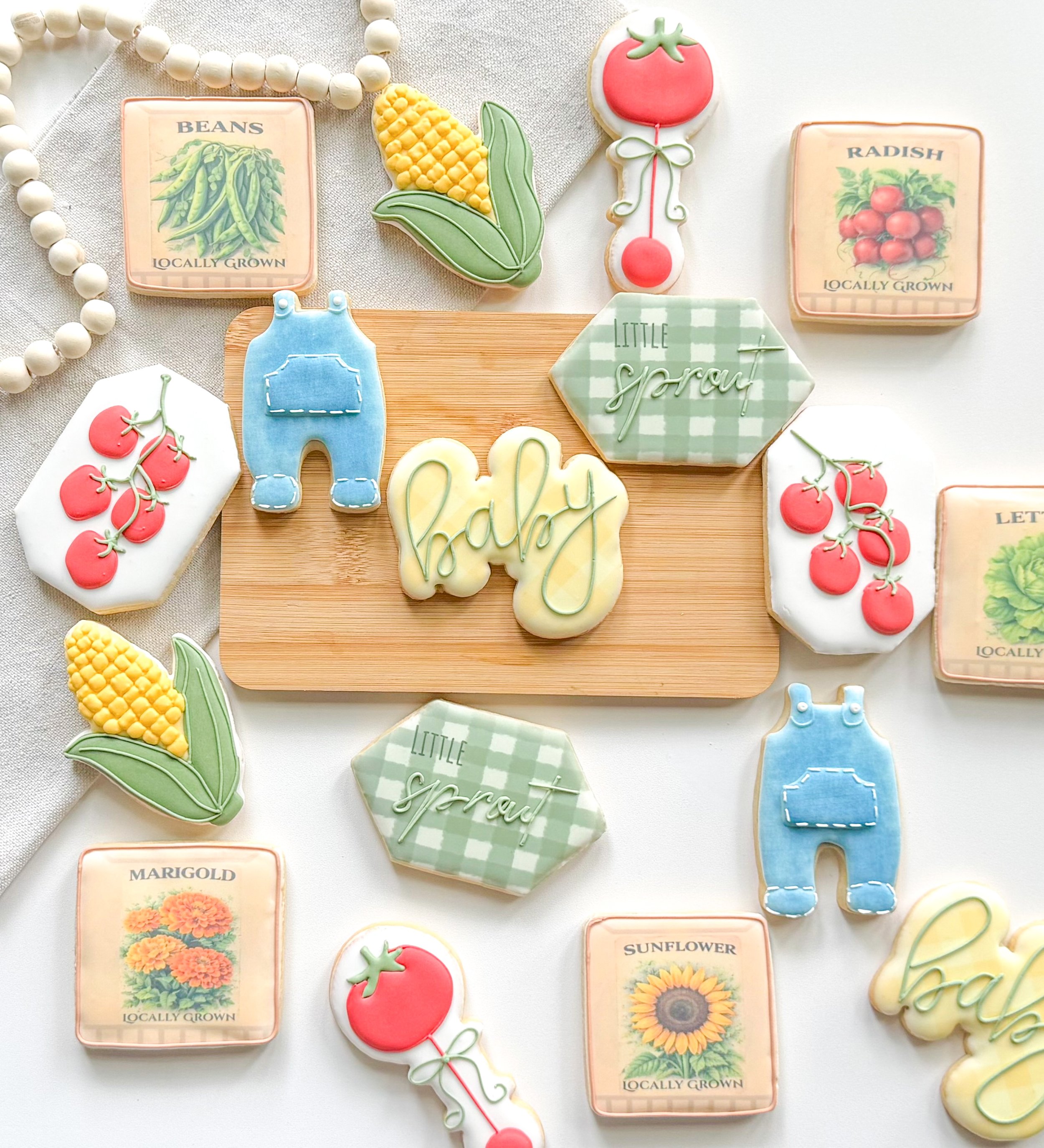 Decorative cookies in the shape of vegetables and flowers with labels such as beans, corn, tomato, sunflower, marigold, radish, and a sign that says "Little Sprout."