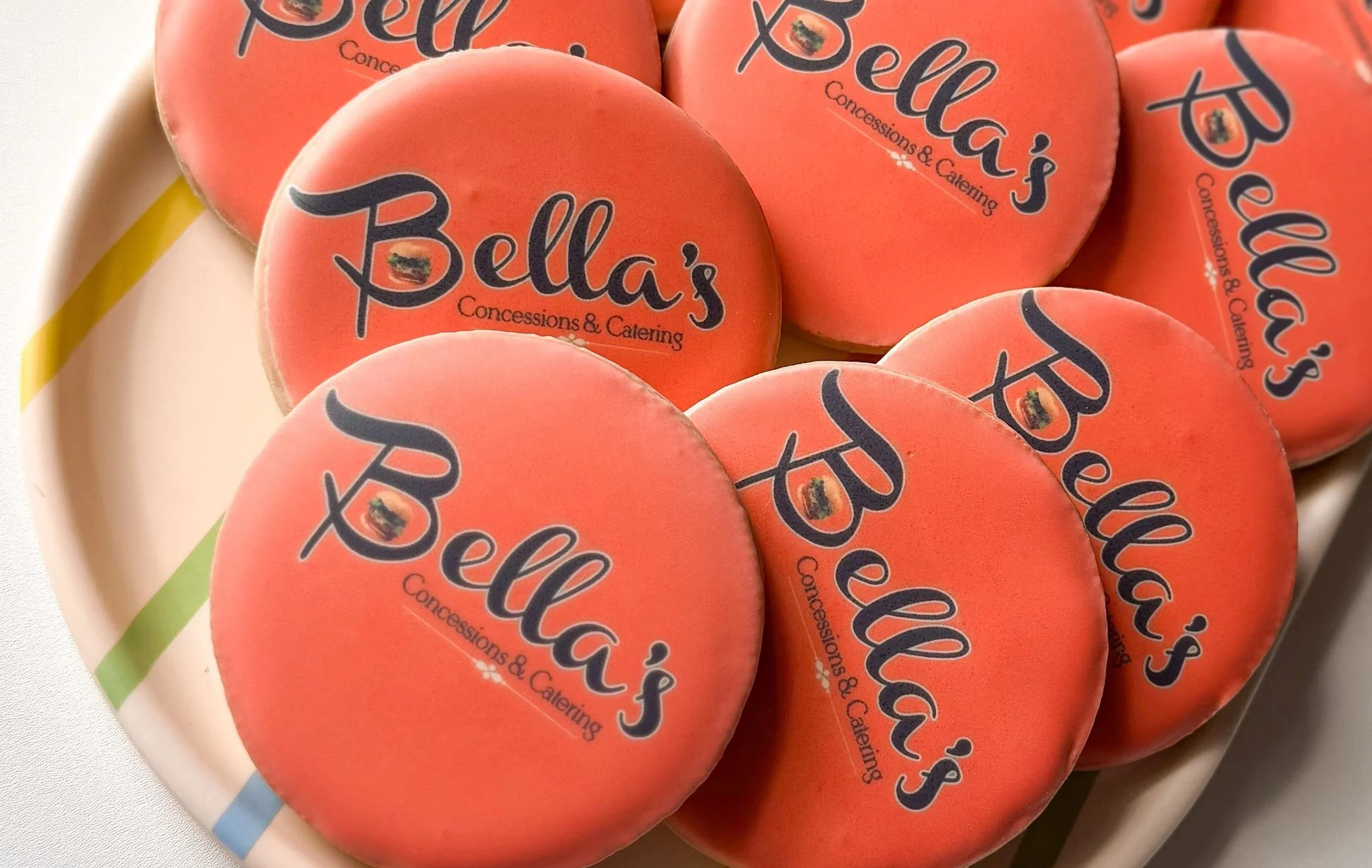 Close-up view of several orange circles with the logo and text 'Bella's Concessions & Catering' printed on them, placed on a white platter.