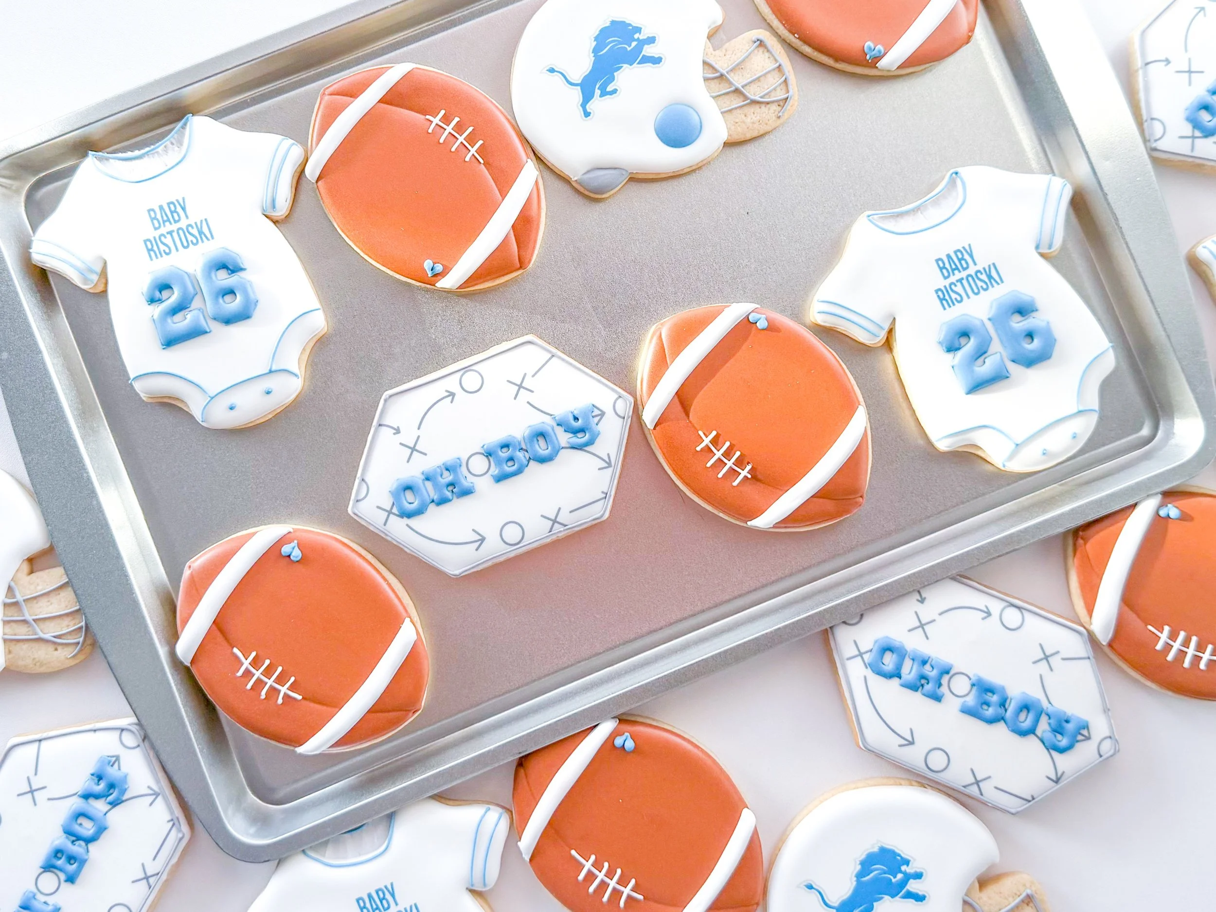 Football-themed baby shower cookies decorated in white, blue, silver, and player uniforms, displayed on a silver tray for a Detroit Lions football team celebration.