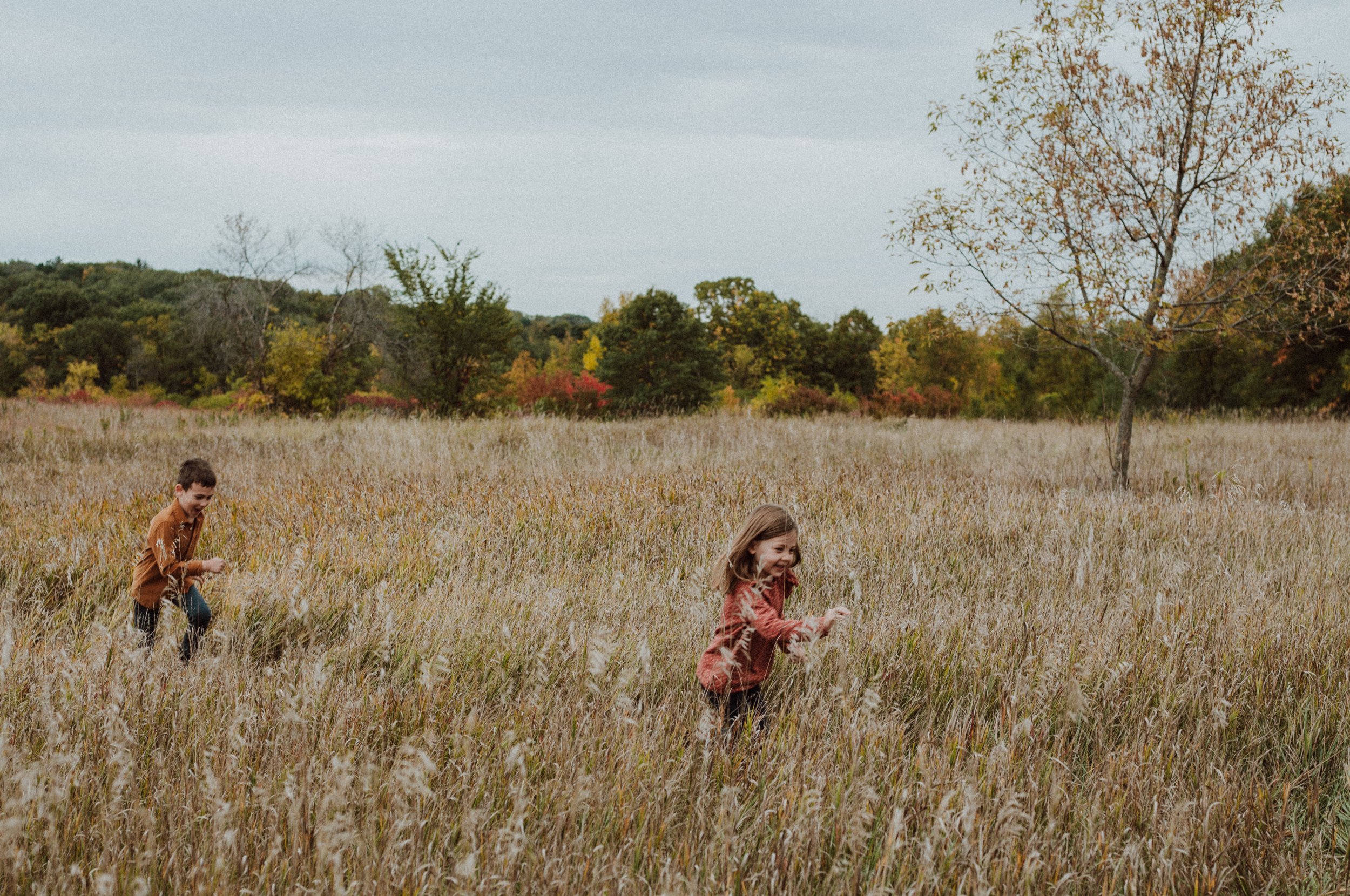 Two siblings running through tall grass during a fall family photo session in Minneapolis