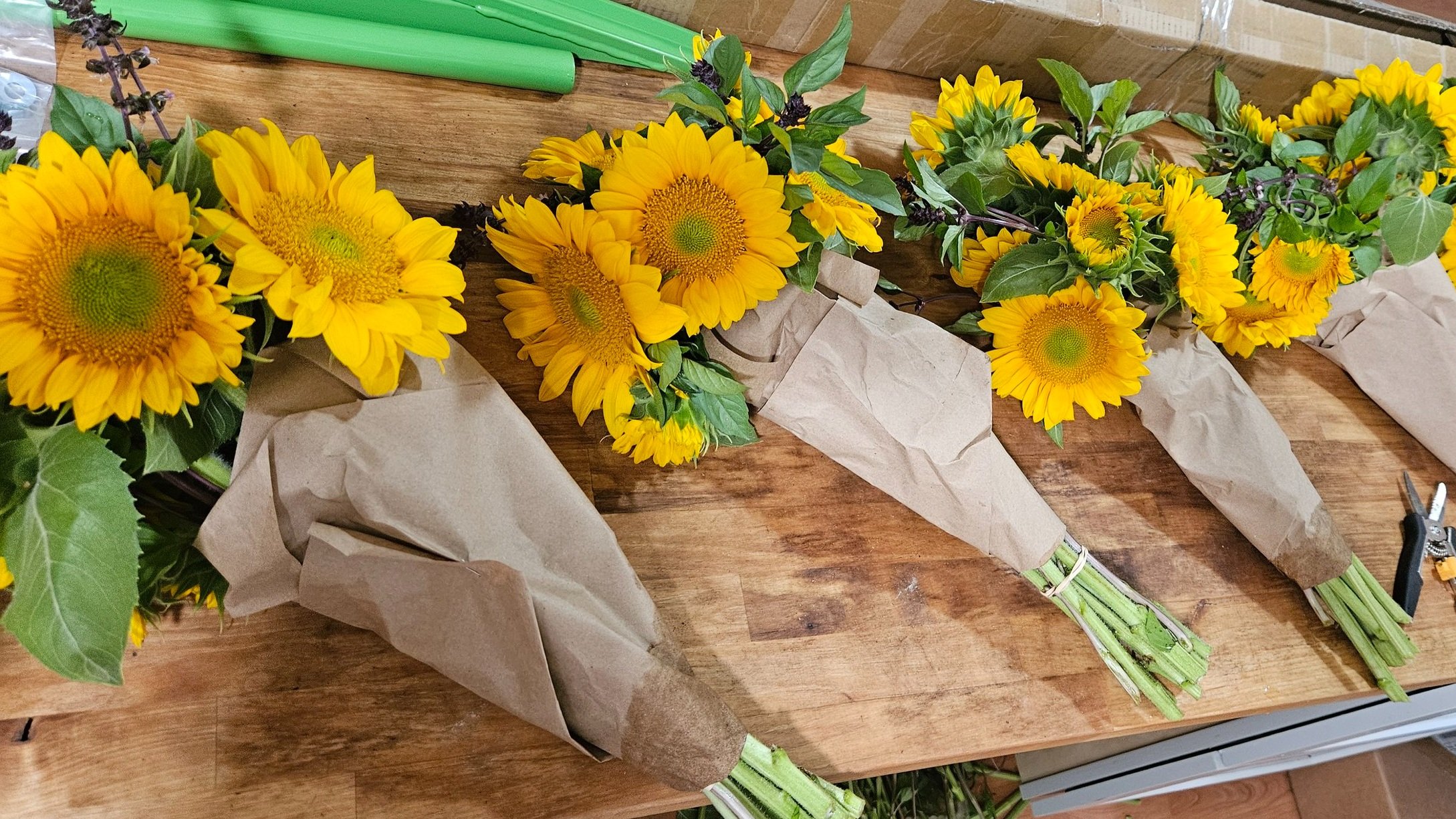 Four bouquets of yellow sunflowers wrapped in brown paper lie on a wooden surface.