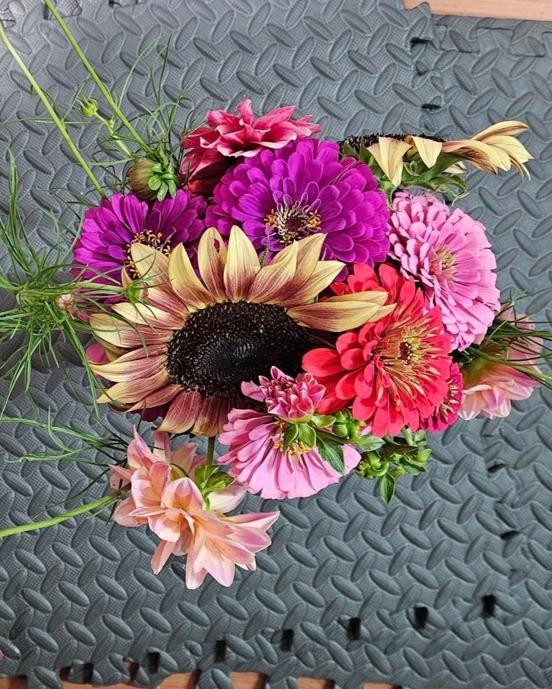 A bouquet of colorful flowers including pink, purple, yellow, and coral blooms resting on a textured gray surface.