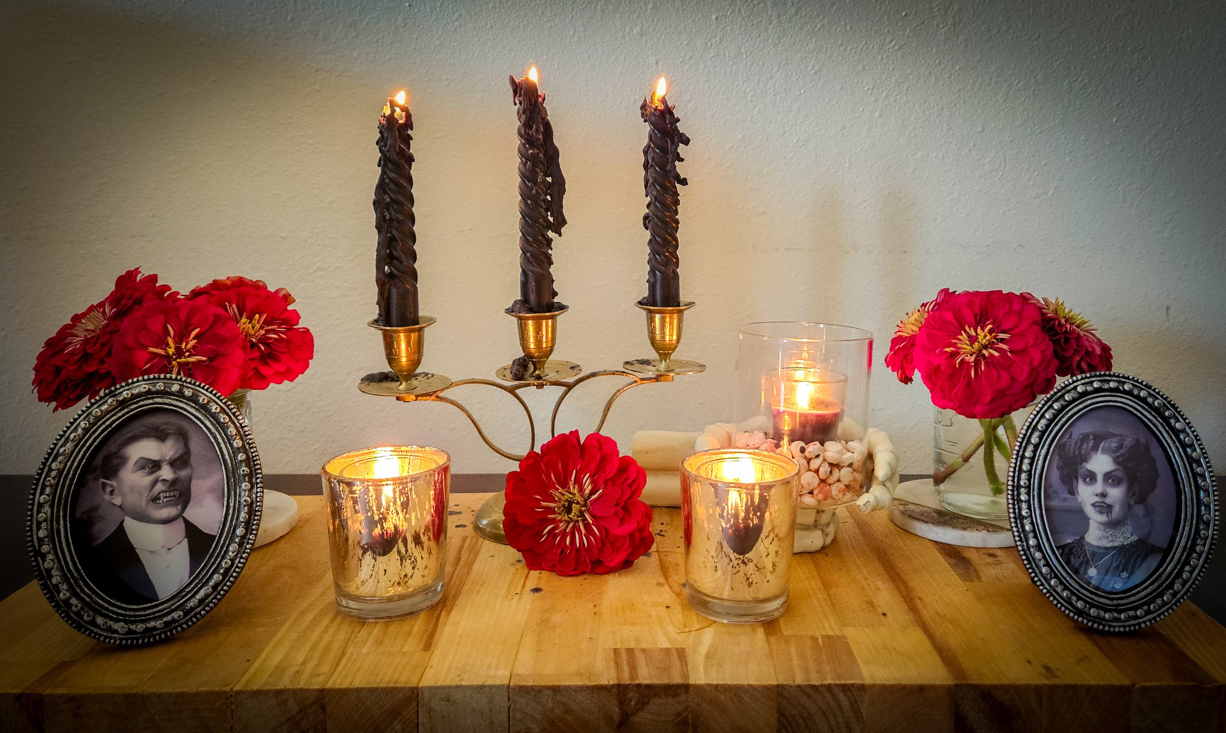 Memorial altar with black candles, red flowers, framed black-and-white photos, and lit candles on a wooden surface.