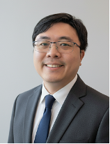 Professional headshot of a smiling man wearing glasses, a dark suit, white shirt, and blue tie.