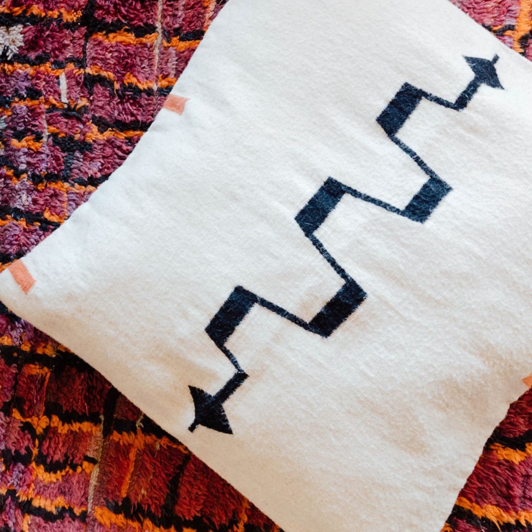 White pillow with black zigzag pattern on colorful textured rug