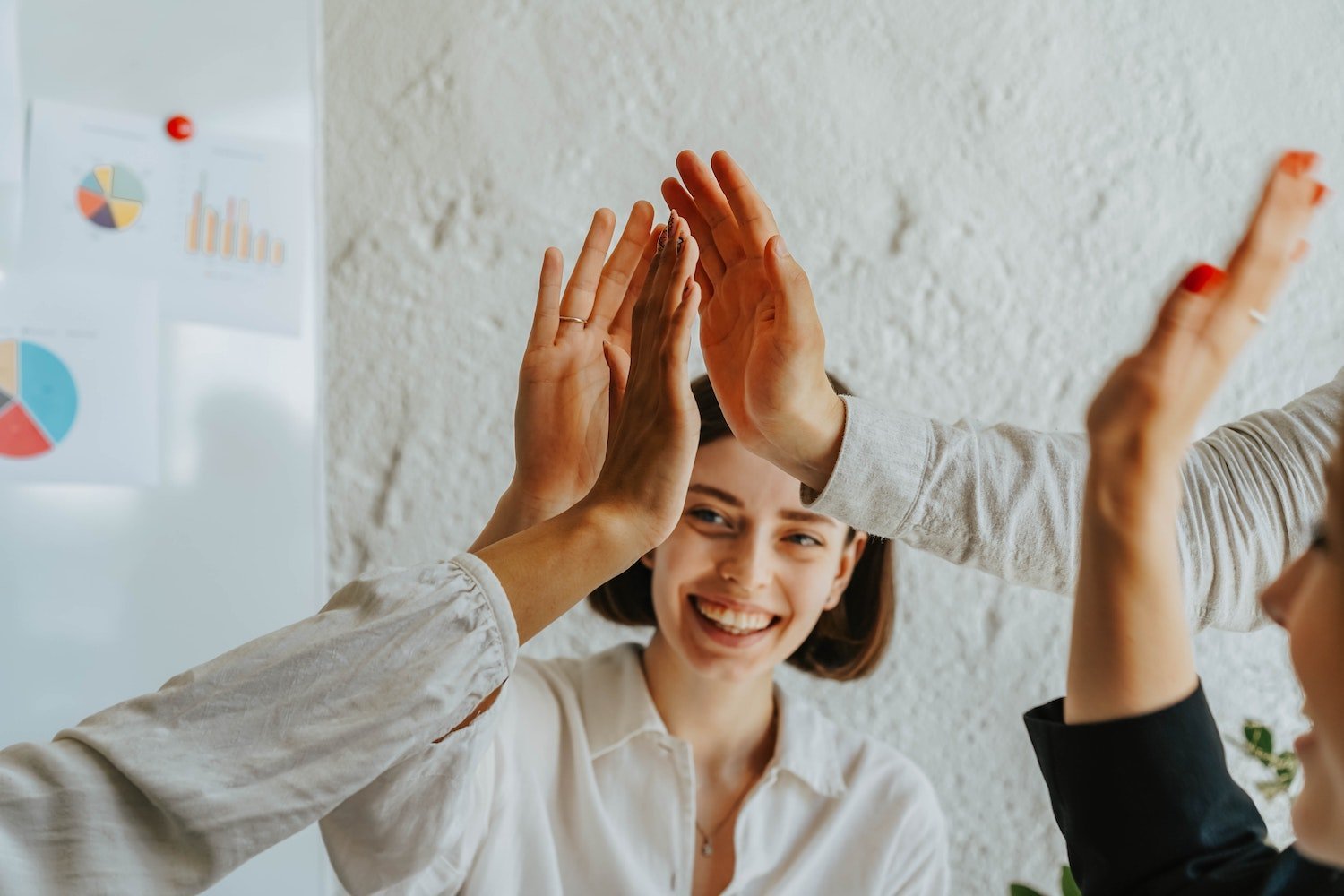 Group of people high-fiving in an office setting with charts on the wall.