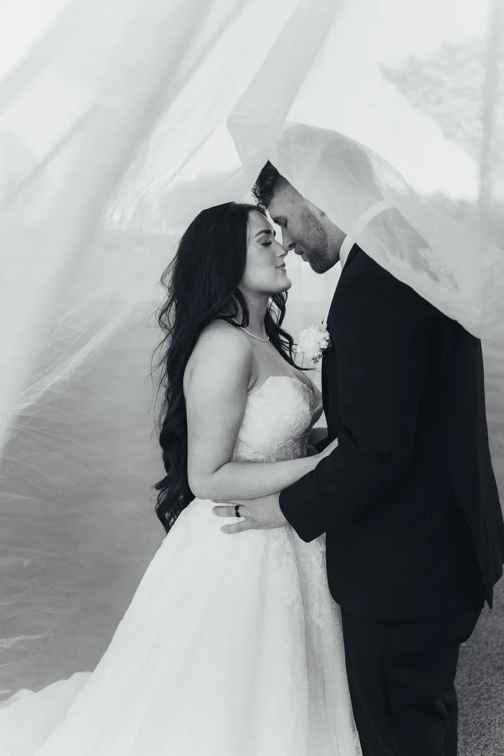 A bride and groom share a romantic moment under a sheer veil on their wedding day.