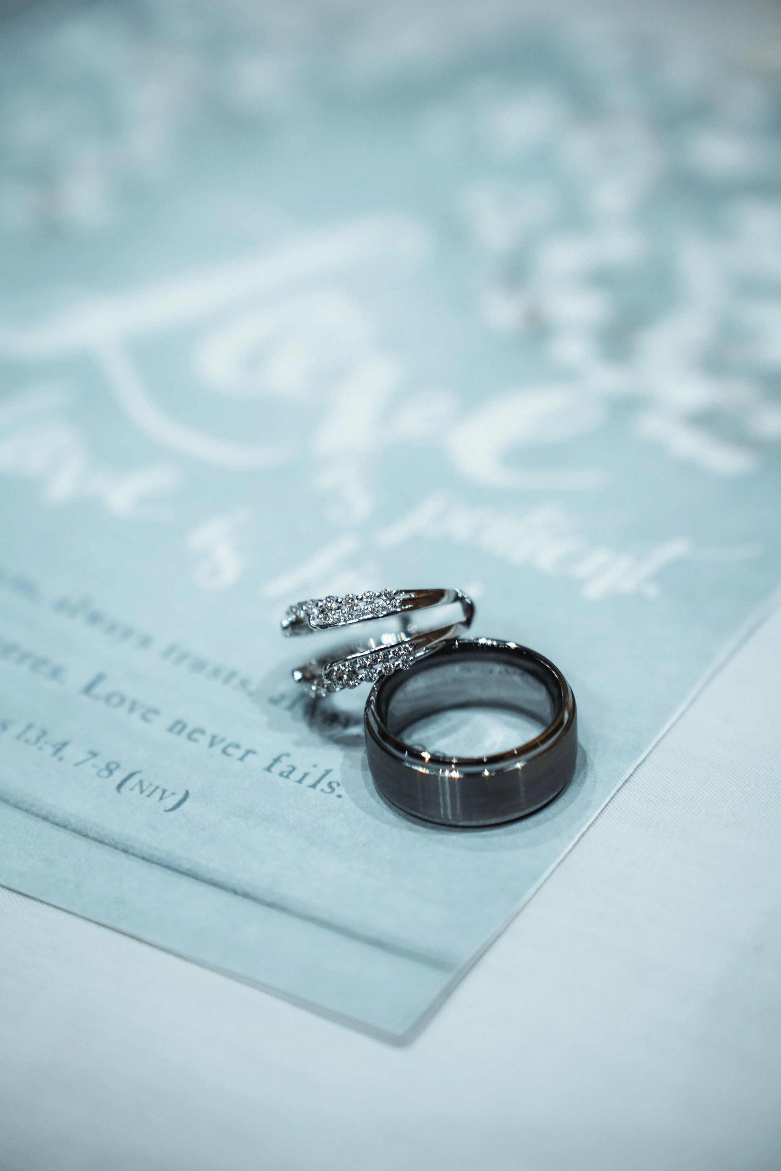 A wedding ring and an engagement ring resting on a wedding invitation with cursive writing.