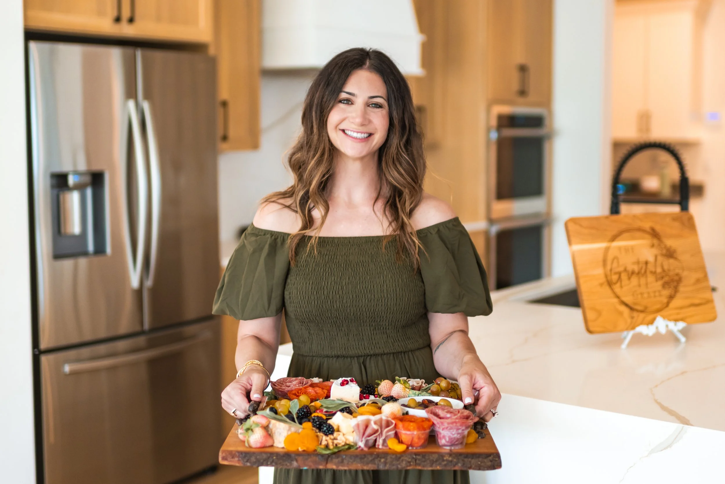 Julie Paul, founder of The Grateful Graze, smiling while crafting a charcuterie board. Jacksonville-based charcuterie expert and catering specialist.