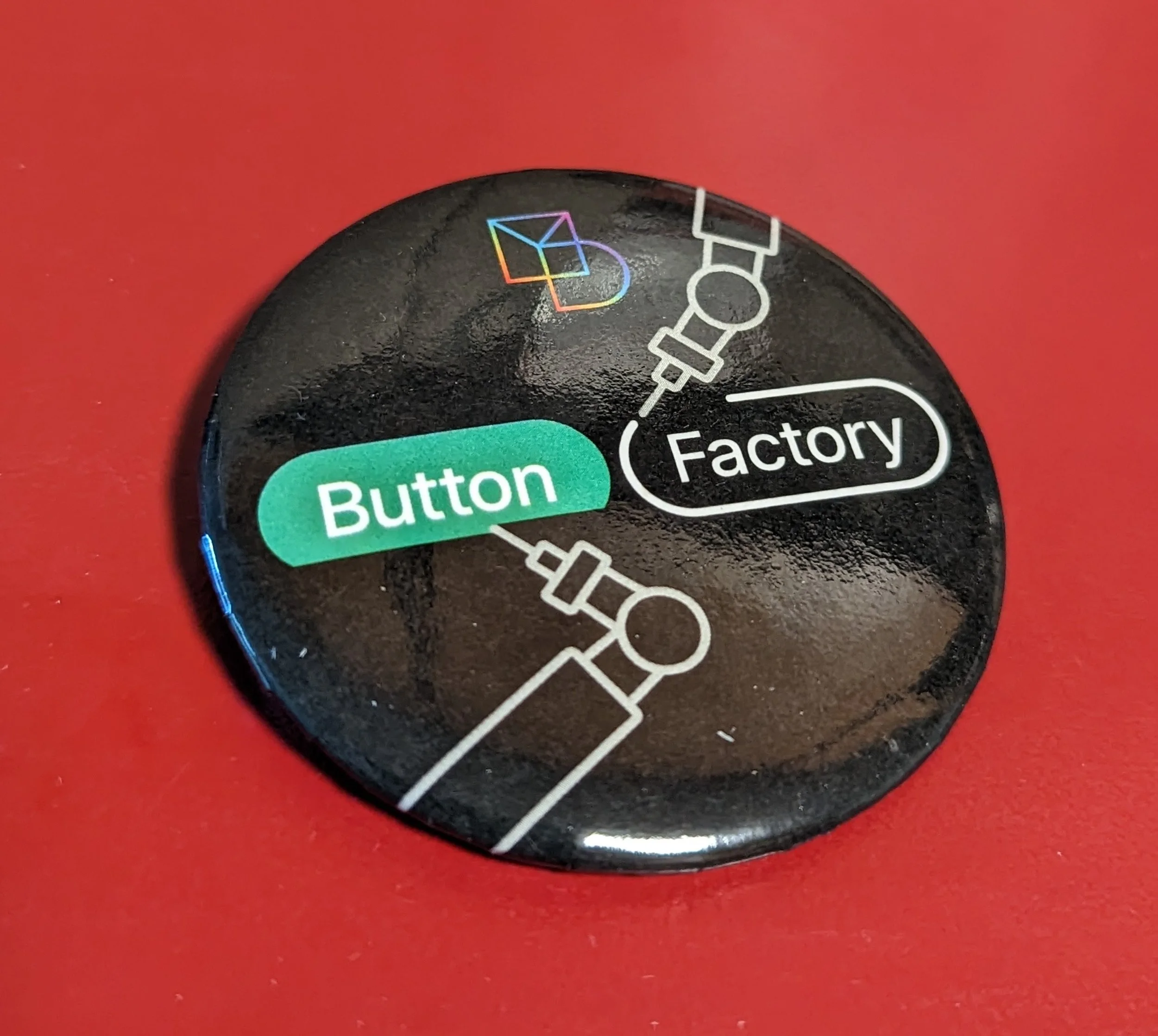 Wearable button pin that shows the Momentum Design logo and the text "Button Factory" written on robotically built buttons