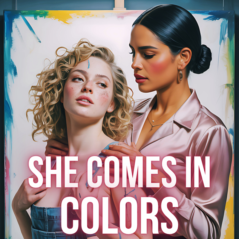 Two women, one with curly blonde hair and the other with slicked-back dark hair, stand closely together in front of an abstract colorful background. The woman with curly hair has a painted dot on her forehead and face, and the woman with dark hair is gently holding her shoulder. Prominent text overlay reads "SHE COMES IN COLORS."