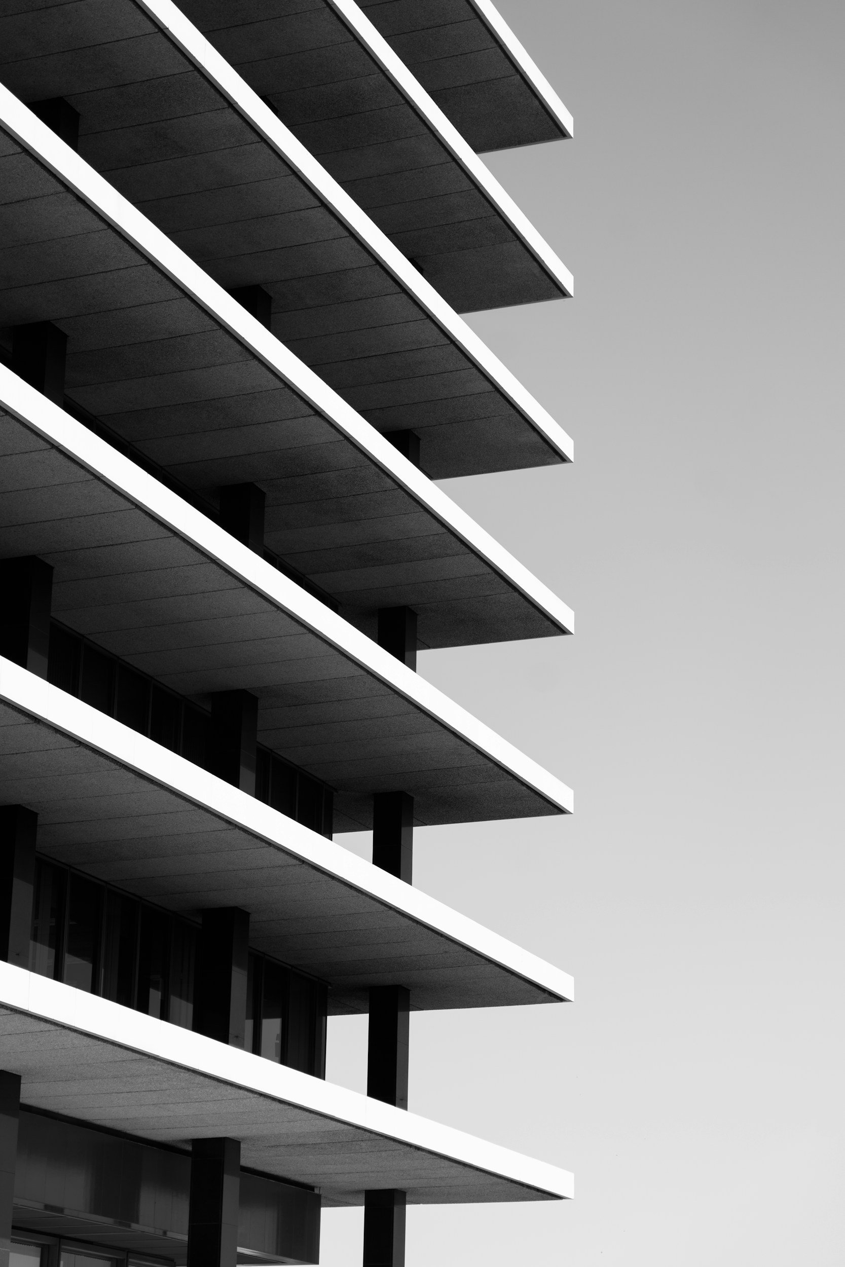 Black and white photo of a modern multi-story building with horizontal balconies and large glass windows, against a clear sky.