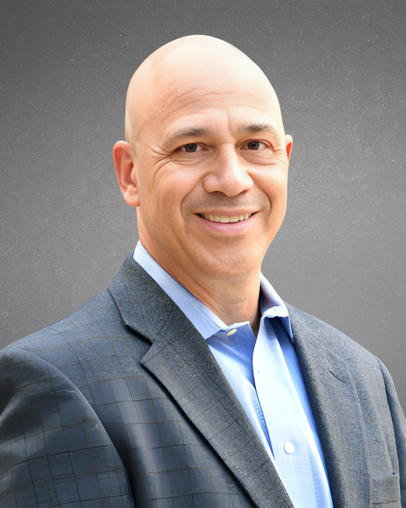 Headshot of Tony Breault, a member of FACTOR's Strategic Advisory Board, wearing a blue dress shirt against a gray background.
