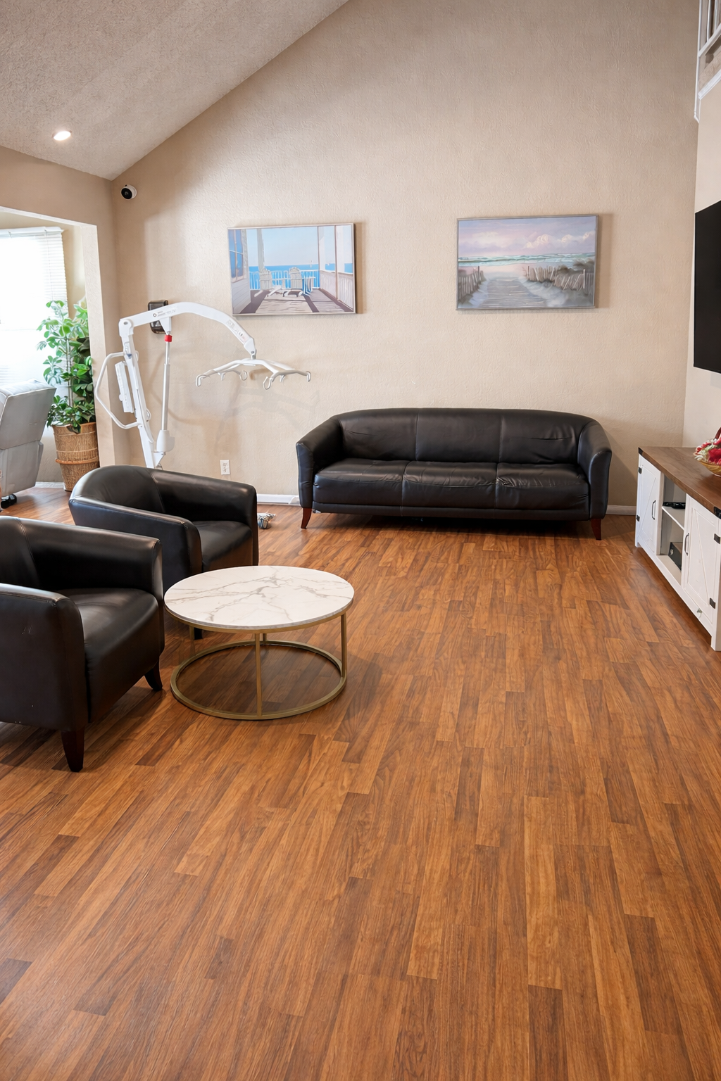 A waiting room with black leather sofas, a white marble round coffee table, wooden flooring, and artwork depicting ocean scenes on the wall.
