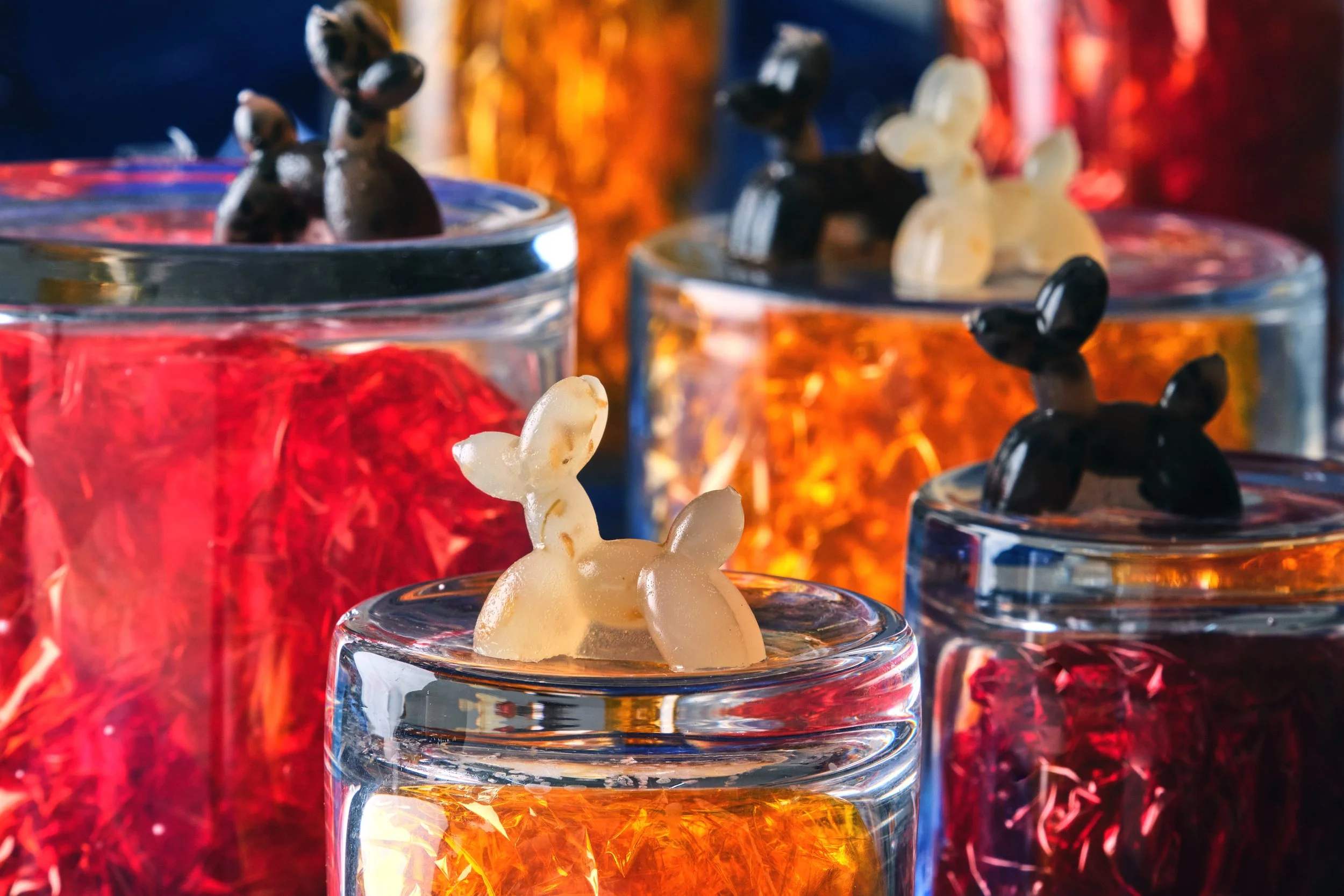 Colorful candles in glass containers with bunny-shaped wax decorations on top.
