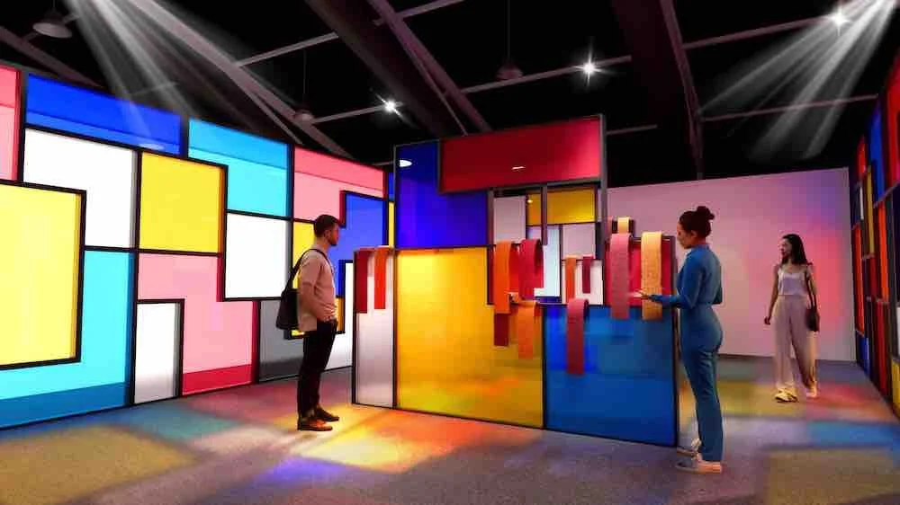 People viewing colorful abstract art installation with geometric shapes and vibrant lighting in an indoor gallery.