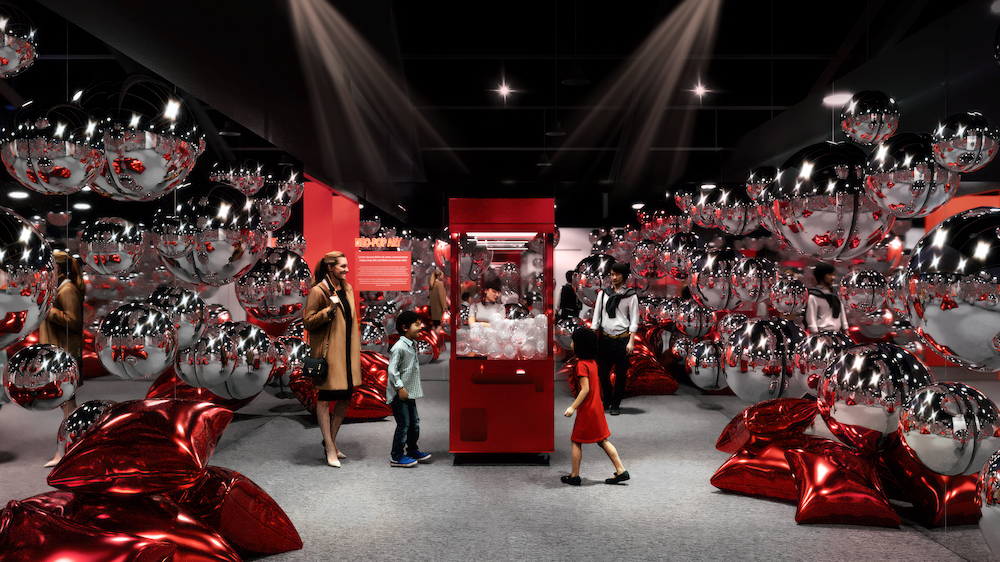 People, including children, viewing a display of shiny silver and red balloons and pillows in a modern exhibit space.