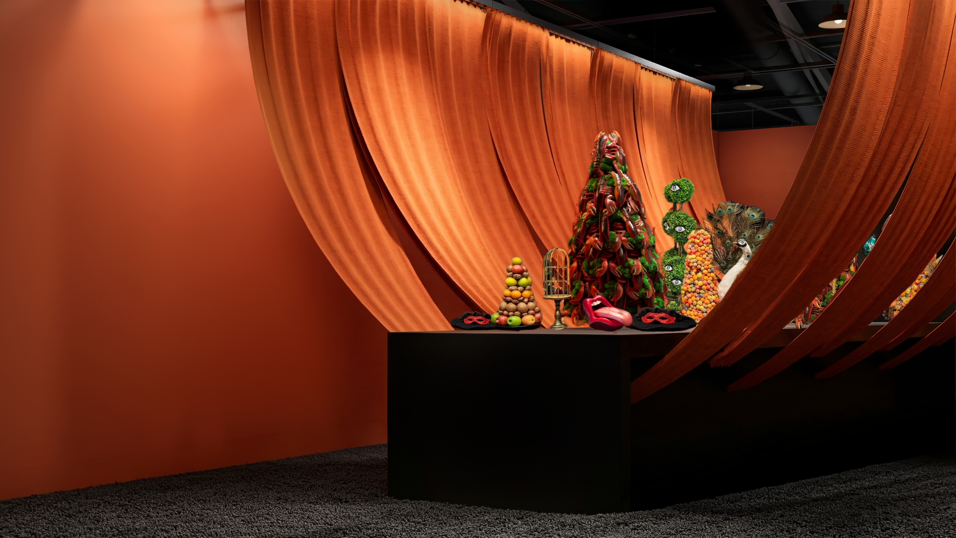 Display of colorful unconventional sculptures and art pieces with a large orange curtain backdrop at an art exhibit.