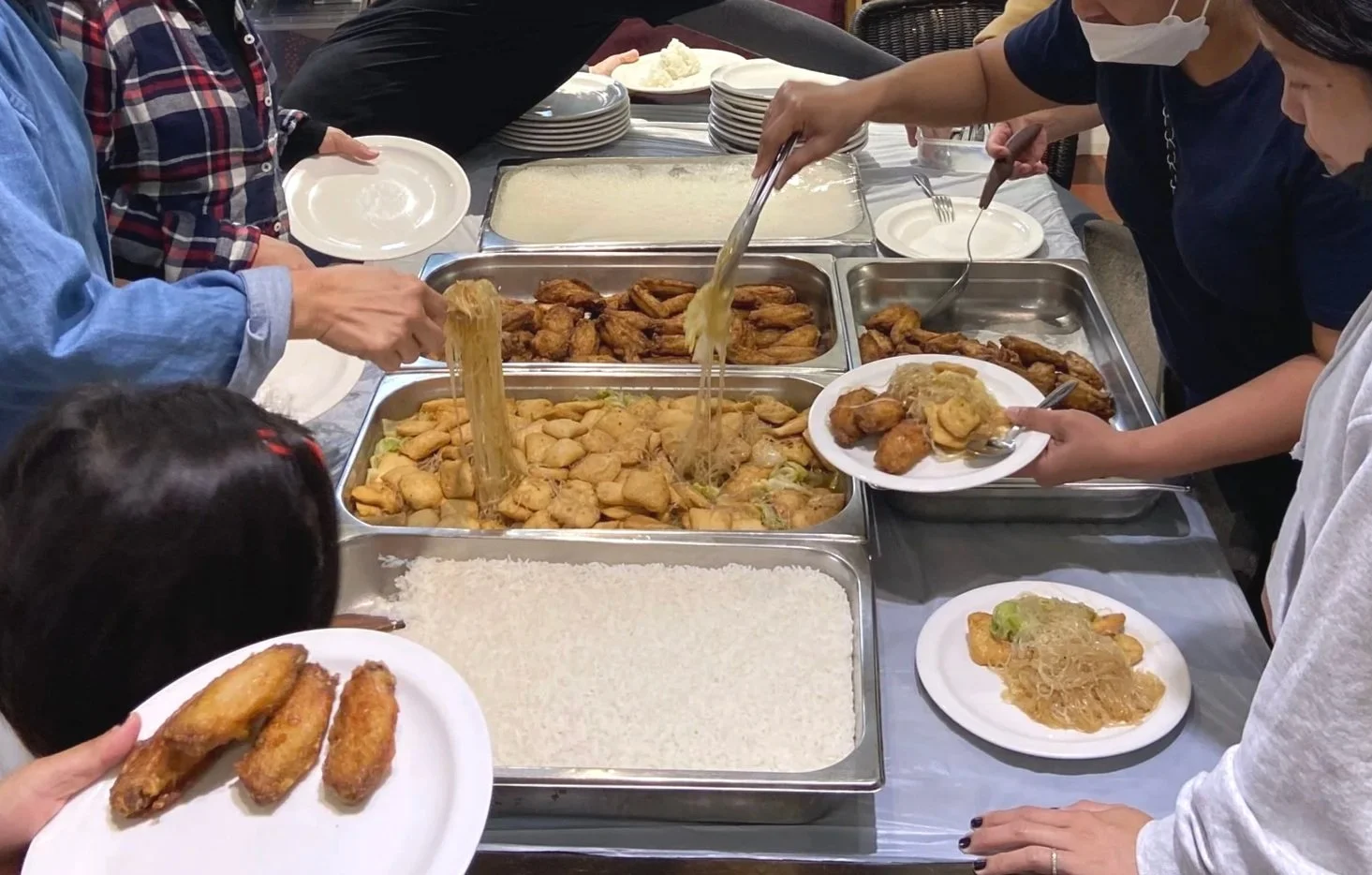 People serving themselves food at a buffet table with fried chicken, rice, and other dishes.