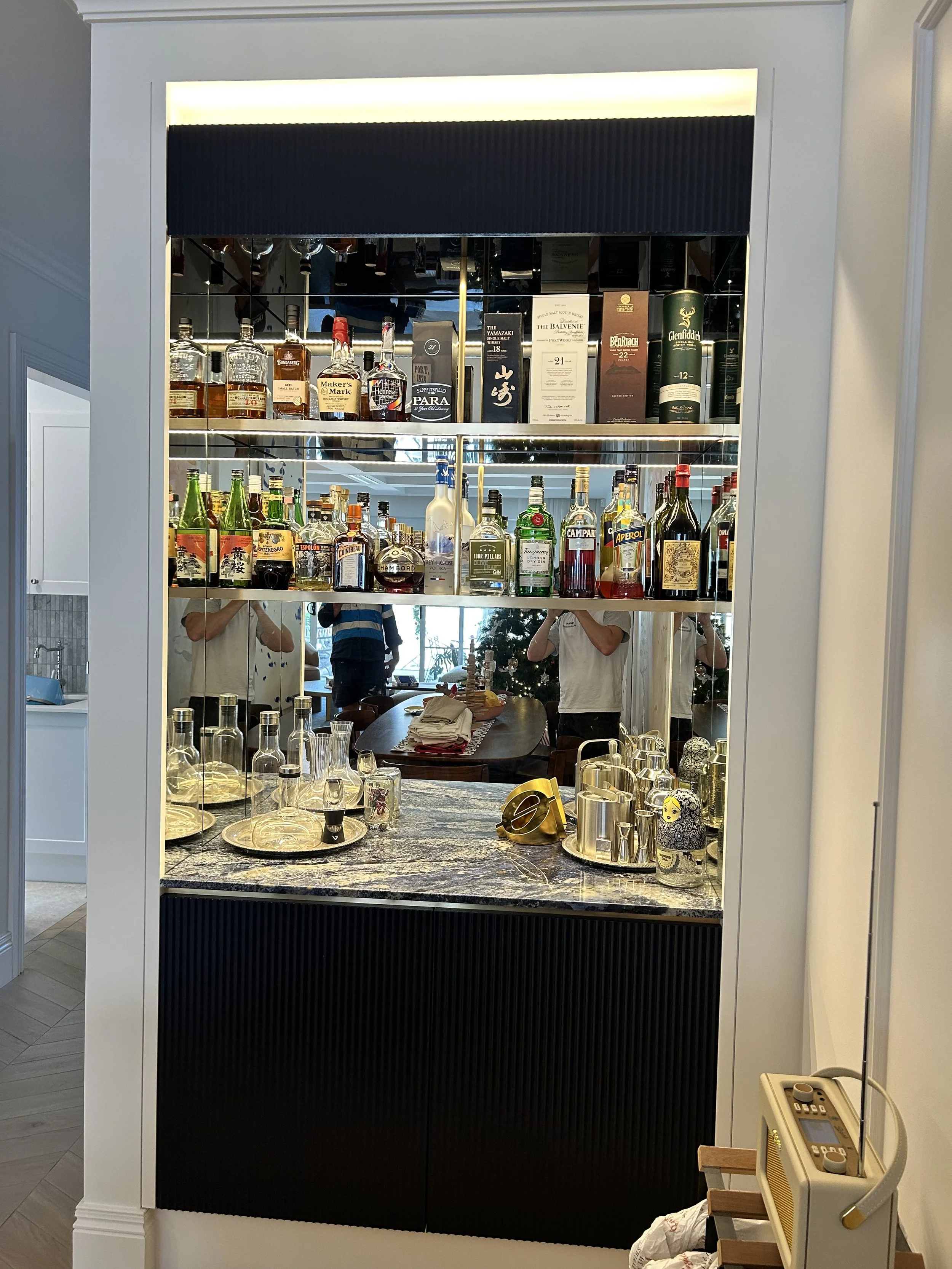 A mirrored bar shelf with various bottles of liquor and glassware in a home or restaurant setting.