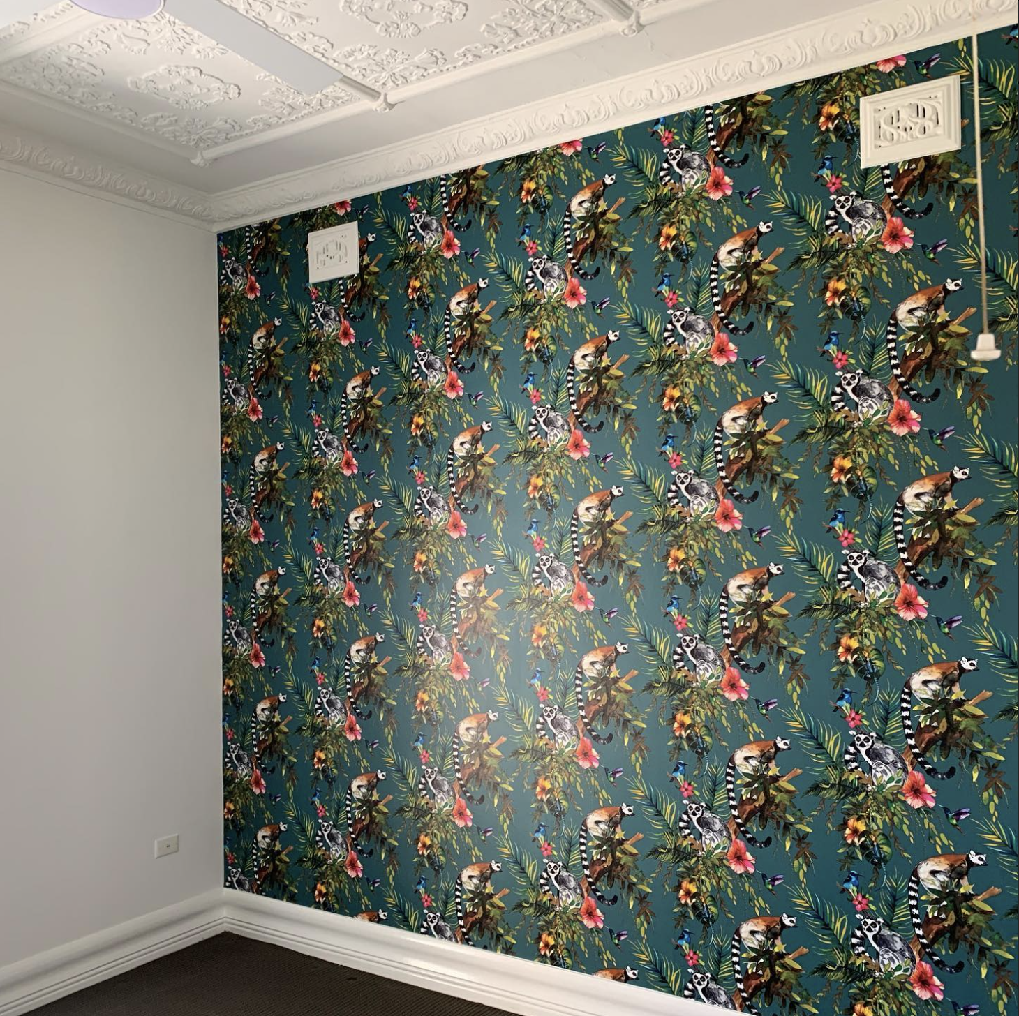 Room with decorative wallpaper featuring lemurs, leaves, and flowers on a blue background, ornate white ceiling, and white molding on walls.