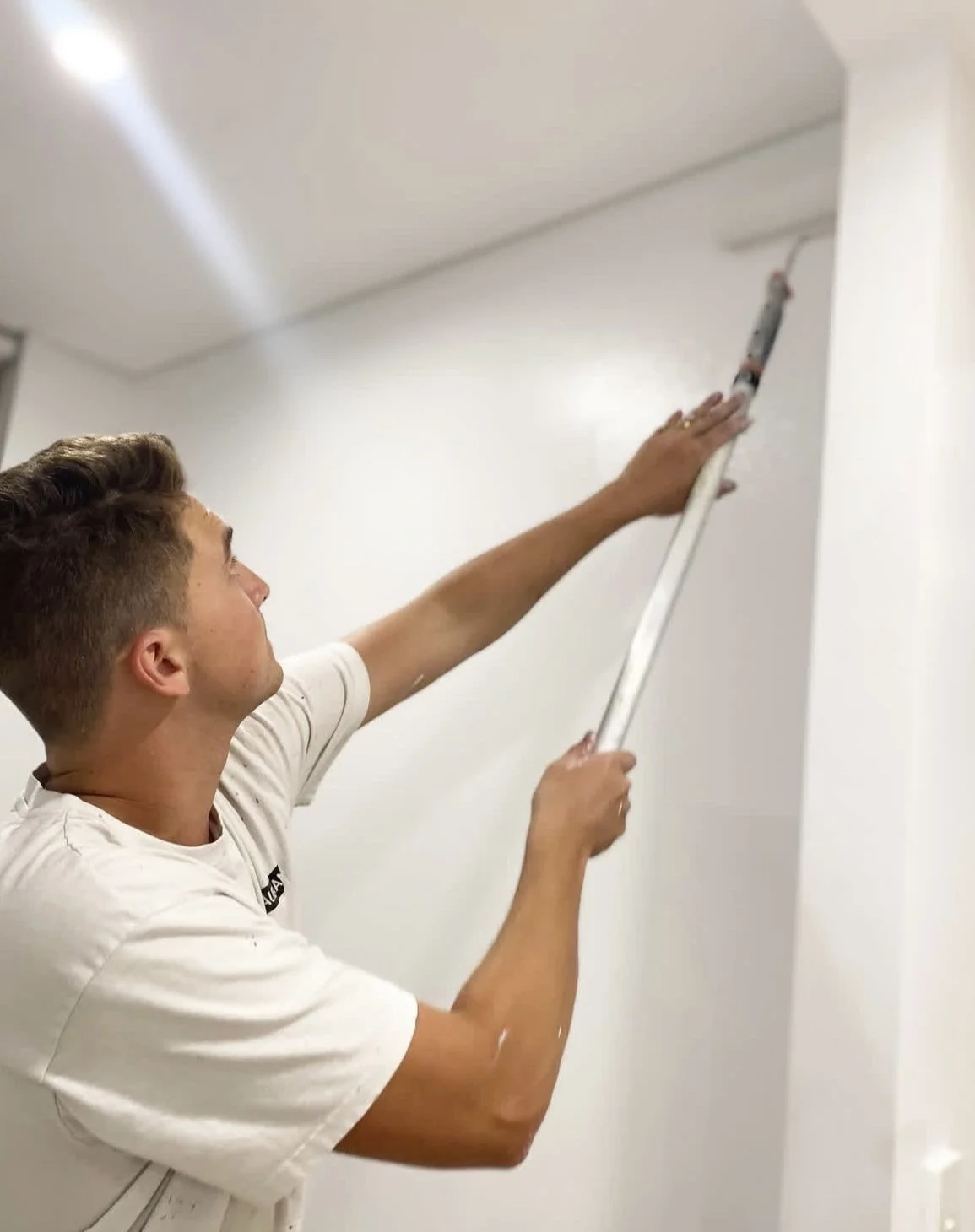 A man using a caulking gun to seal the corner of a white wall and ceiling.