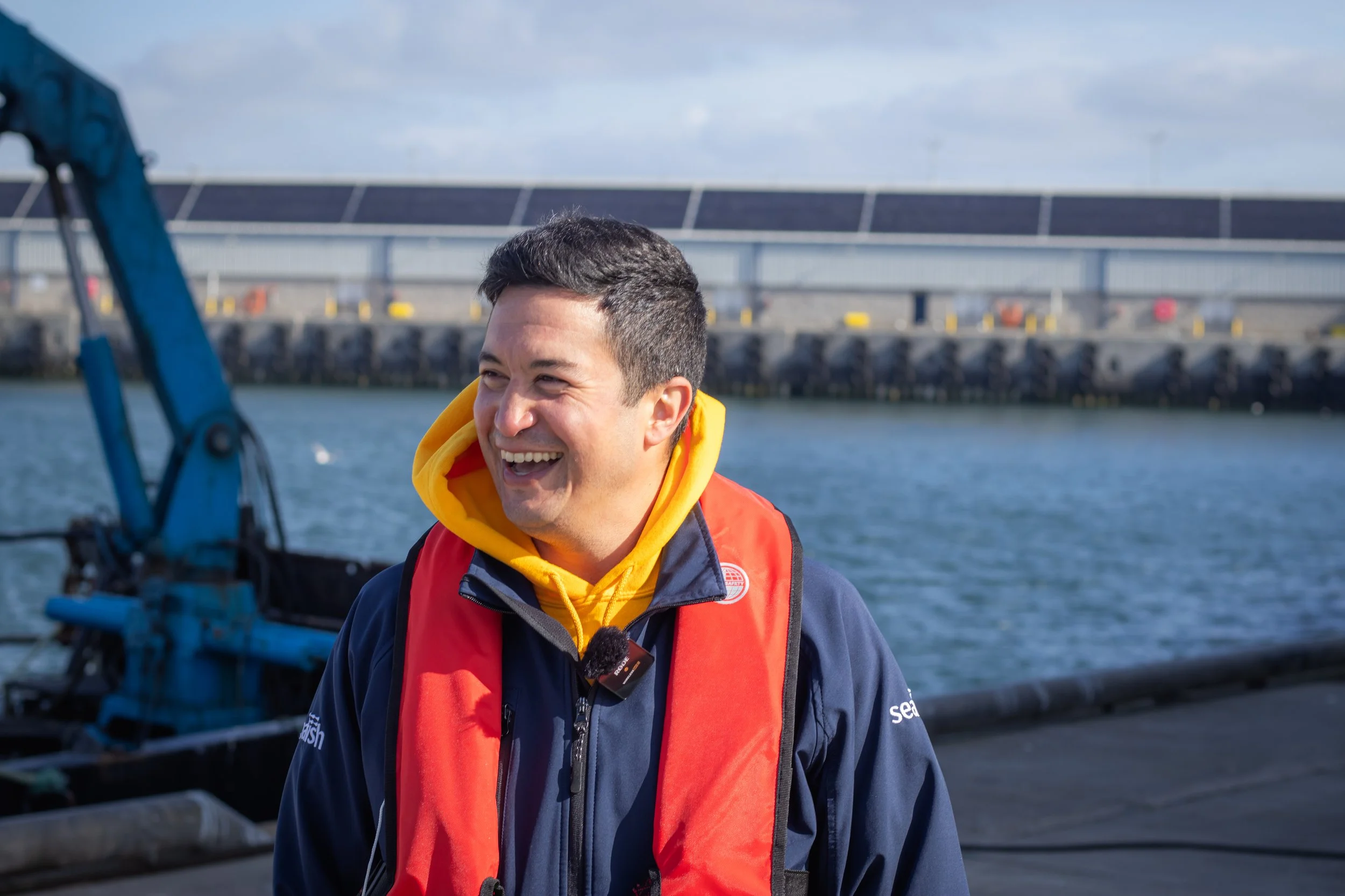 A man in a PFD smiling in front of a harbor