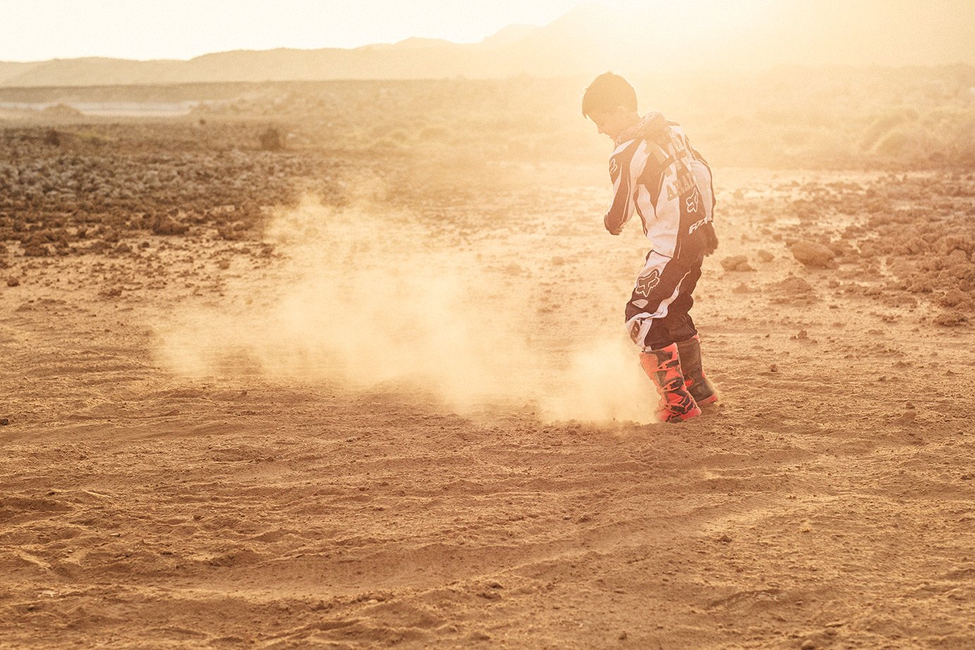 Boy in motocross leathers having fun kicking dirt in the desert.