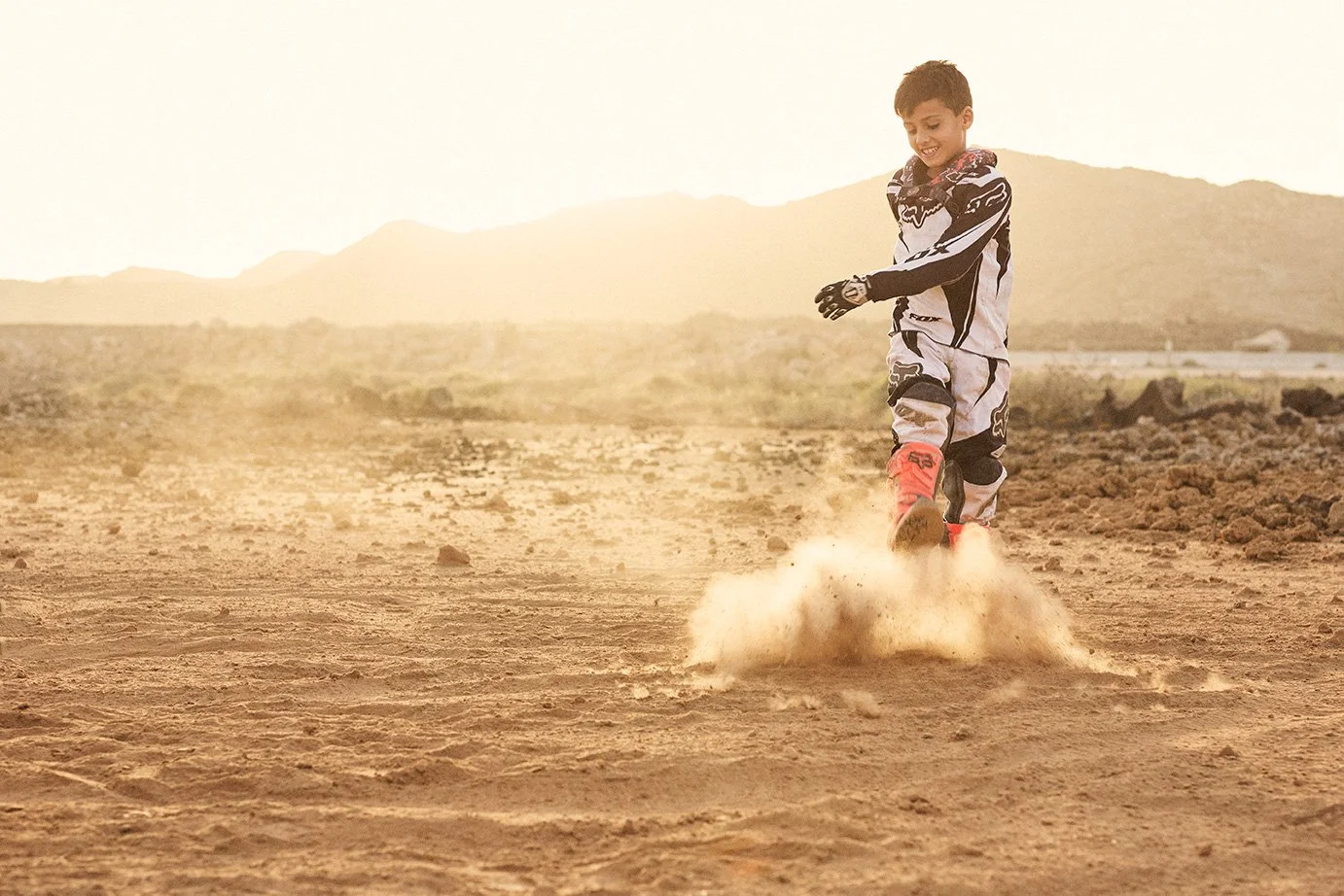 A young boy in motocross leathers kicking the dust in a desert type environment in the Canary Islands.