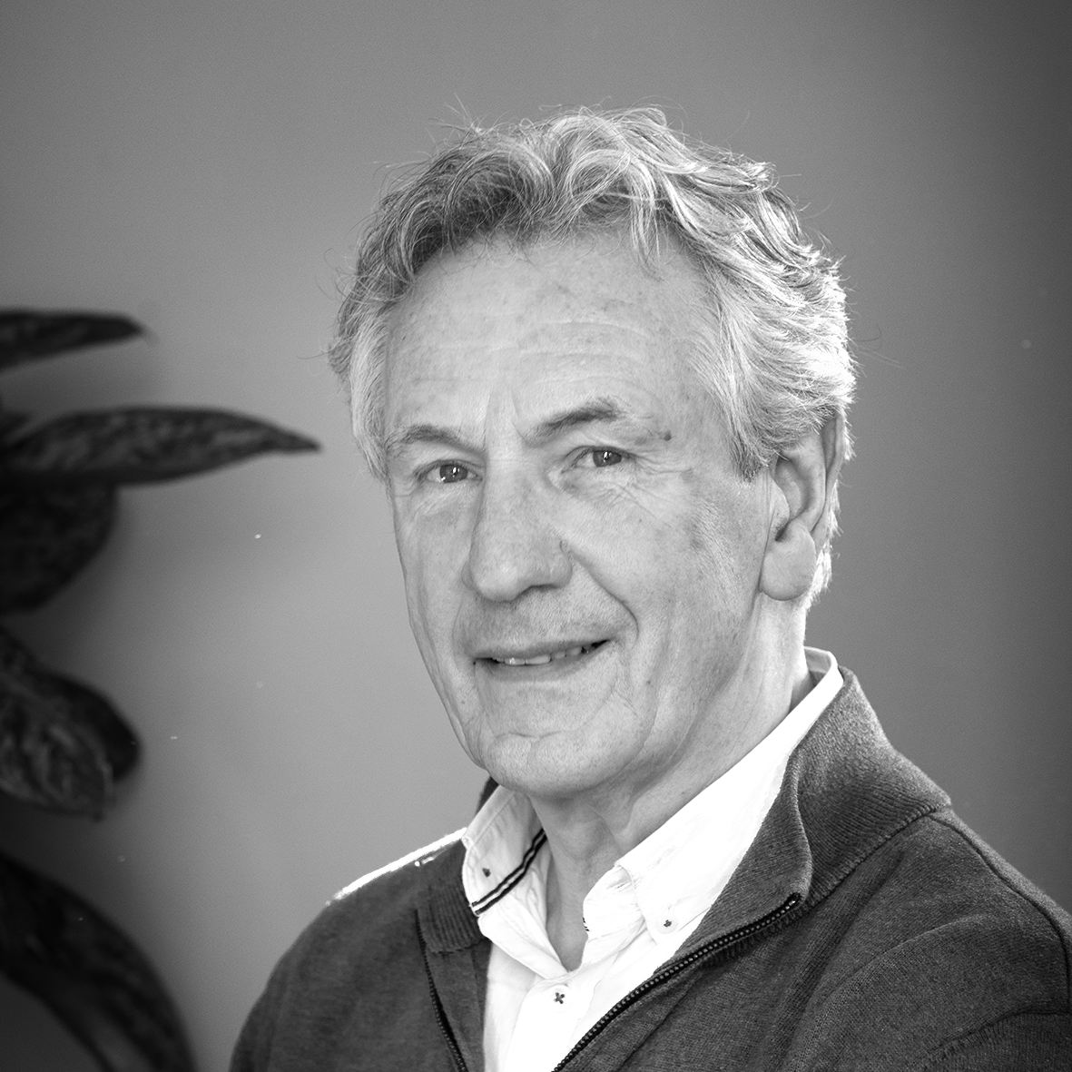 Elderly man with gray hair smiling in a black and white portrait, wearing a collared shirt and sweater.